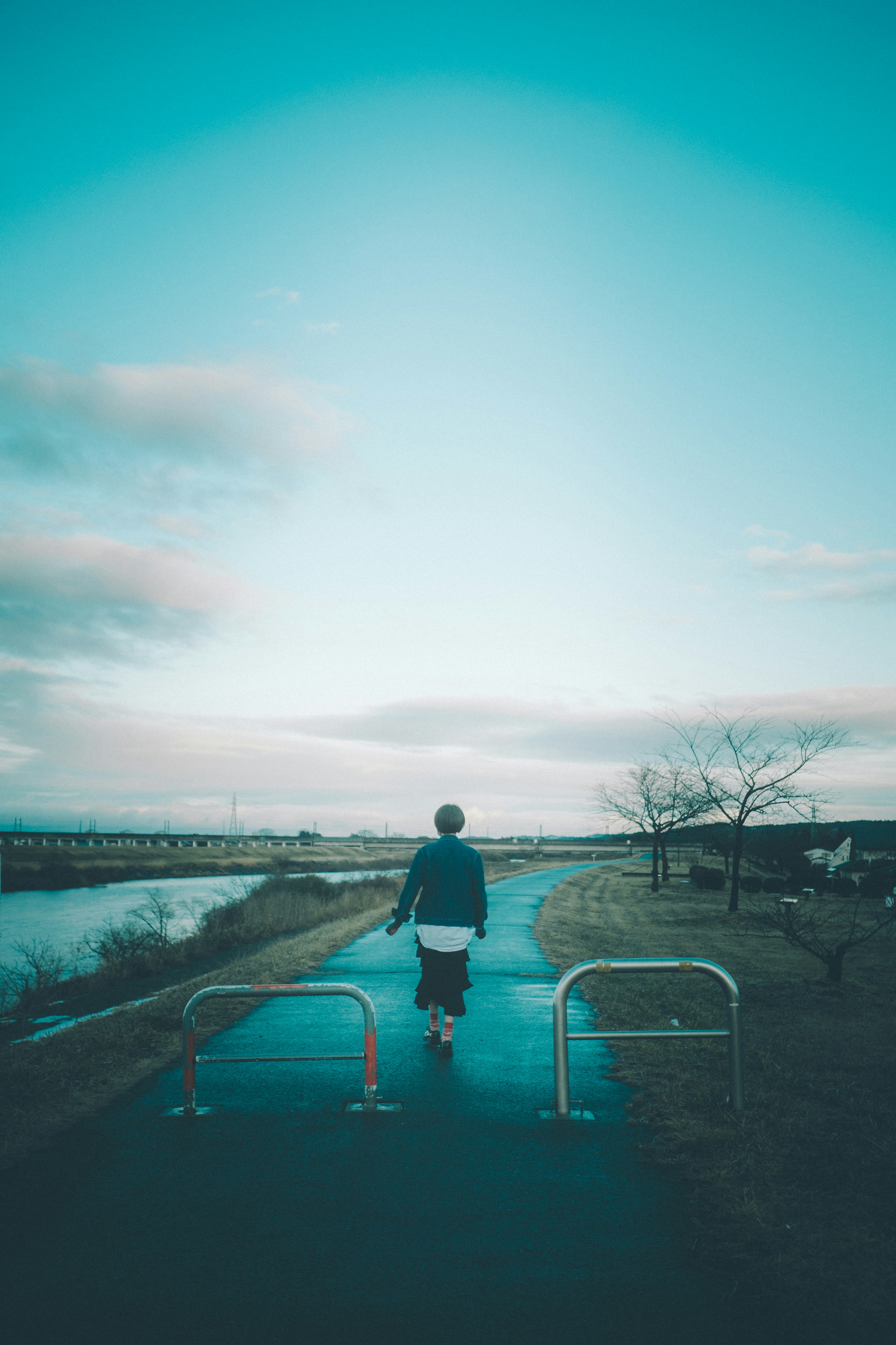 Person walking away on a path by a river under a blue sky