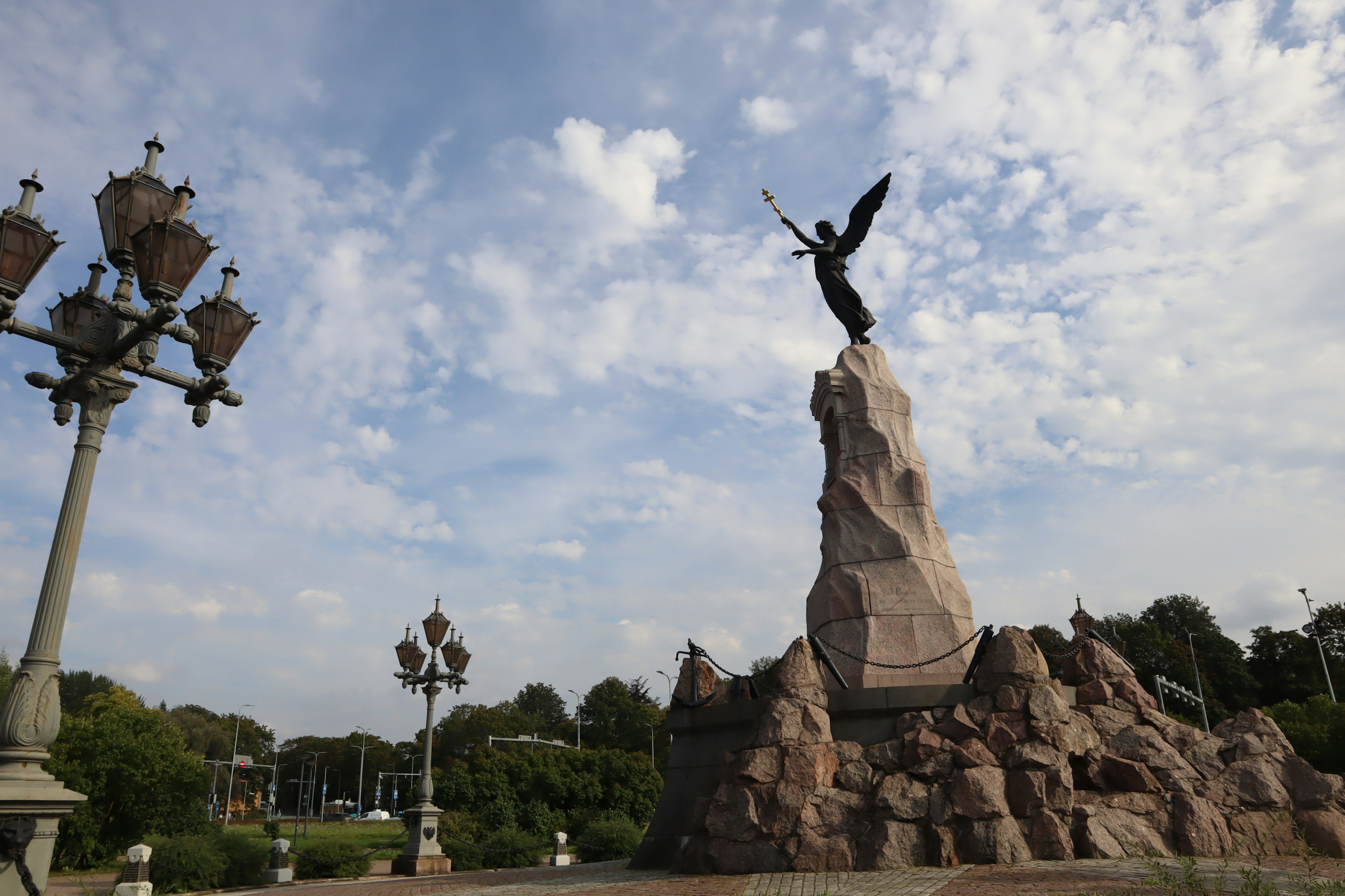 Statua di un angelo su un piedistallo di roccia in un parco con lampioni decorativi