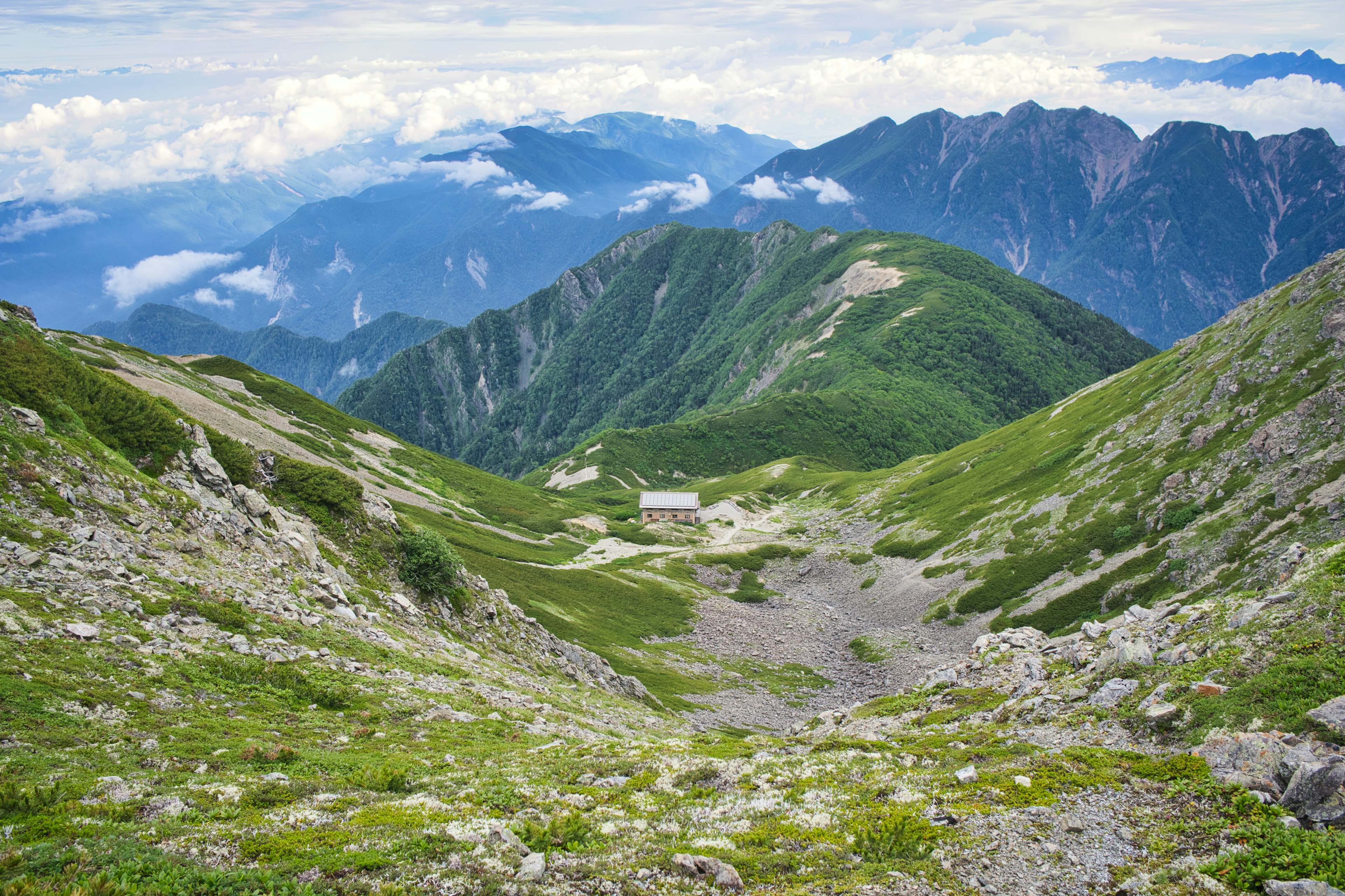 緑の山々と谷間に囲まれた風景に小さな建物が見える