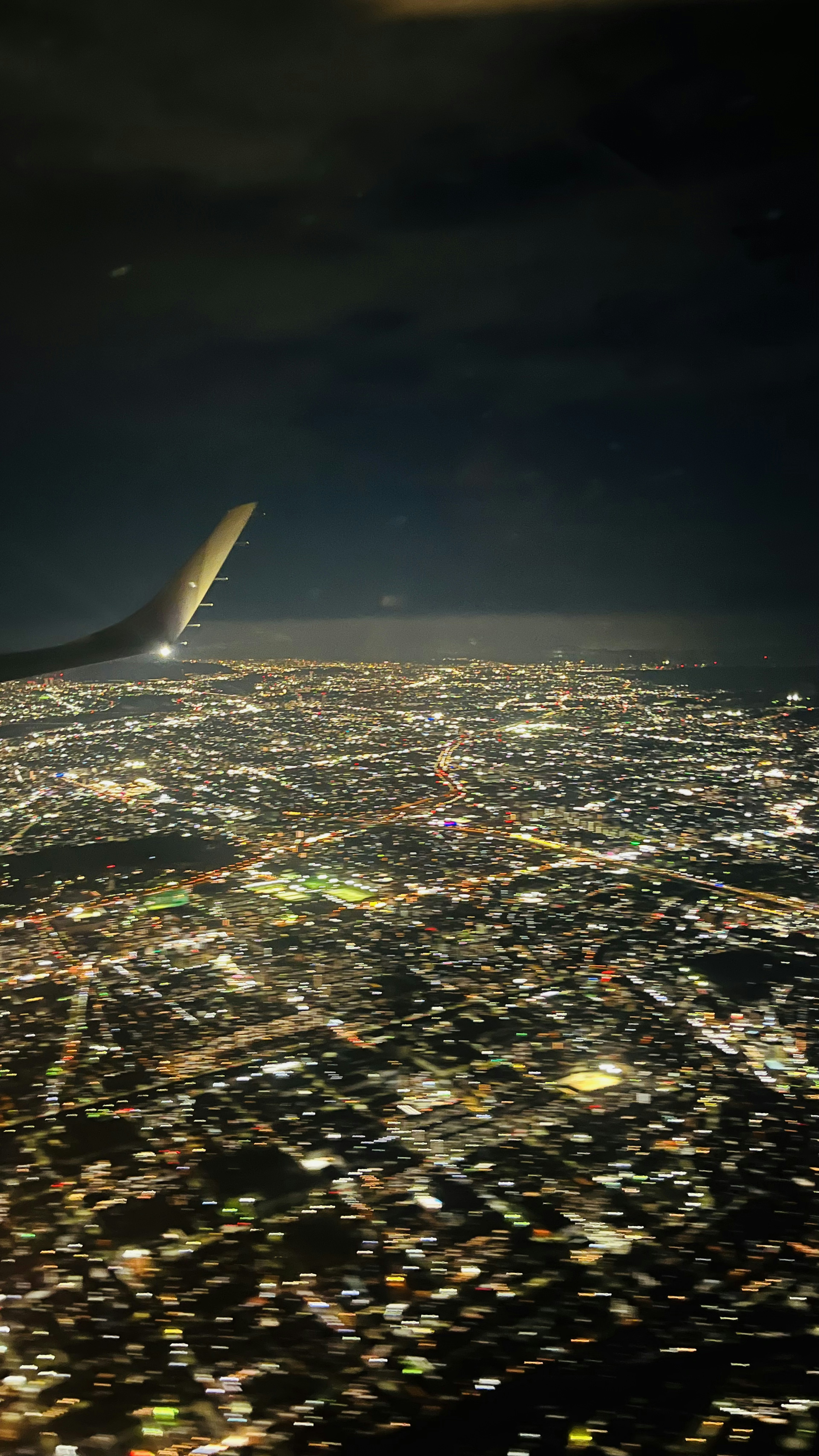 Vue aérienne d'une ville la nuit avec une aile d'avion visible