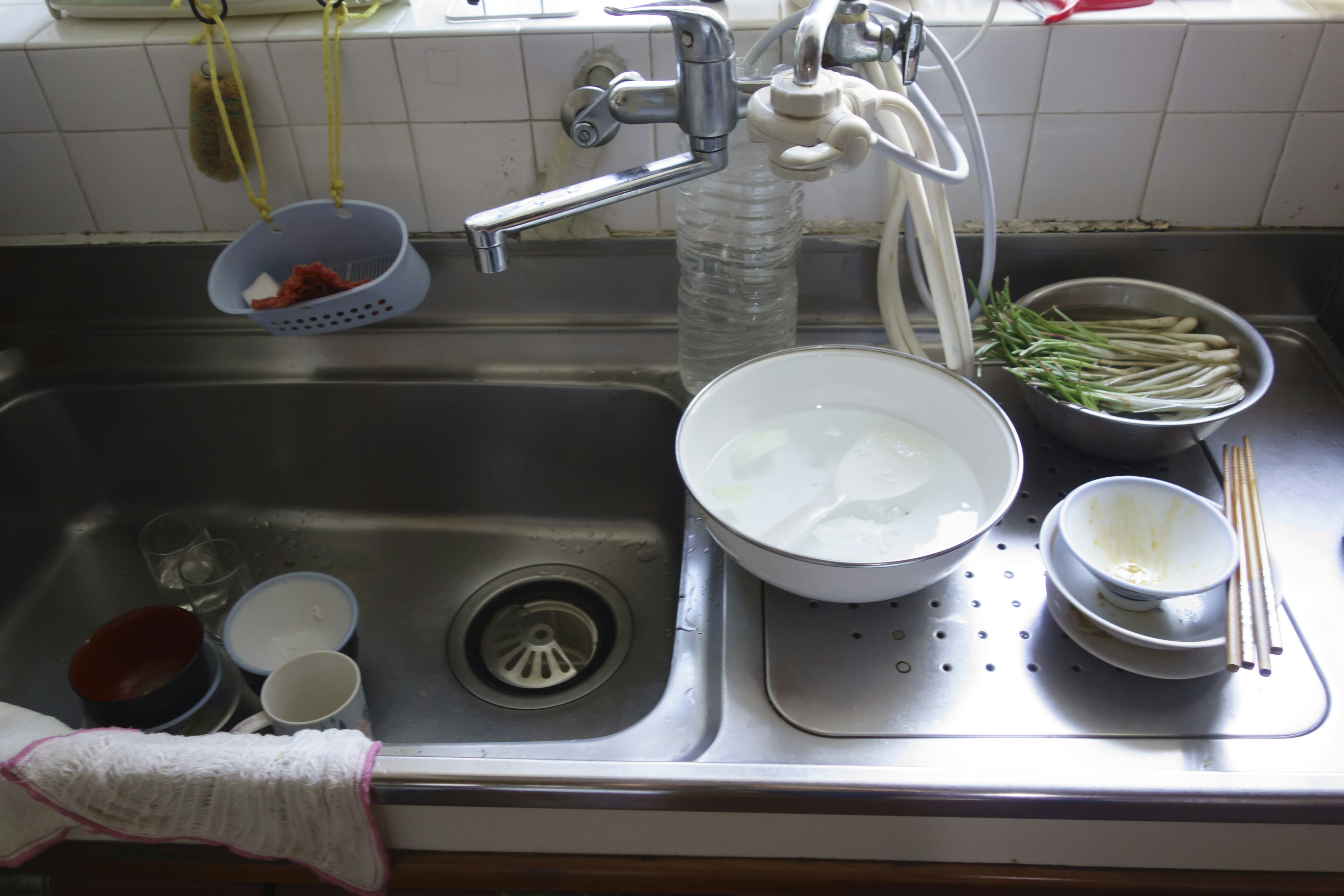 A kitchen sink with various dishes and ingredients A bowl filled with water and dirty dishes are prominent