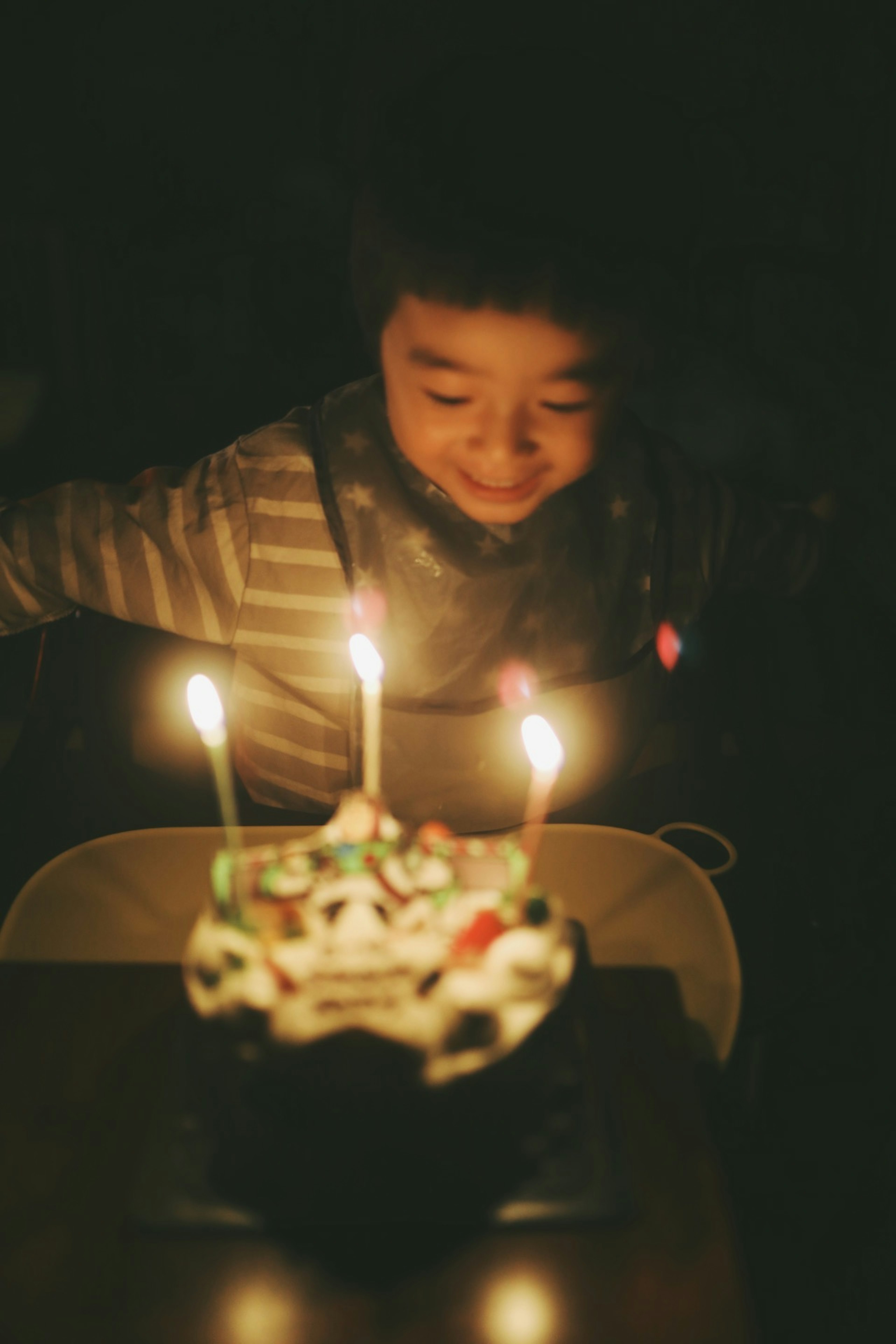 Anak tersenyum di depan kue ulang tahun dengan lilin menyala