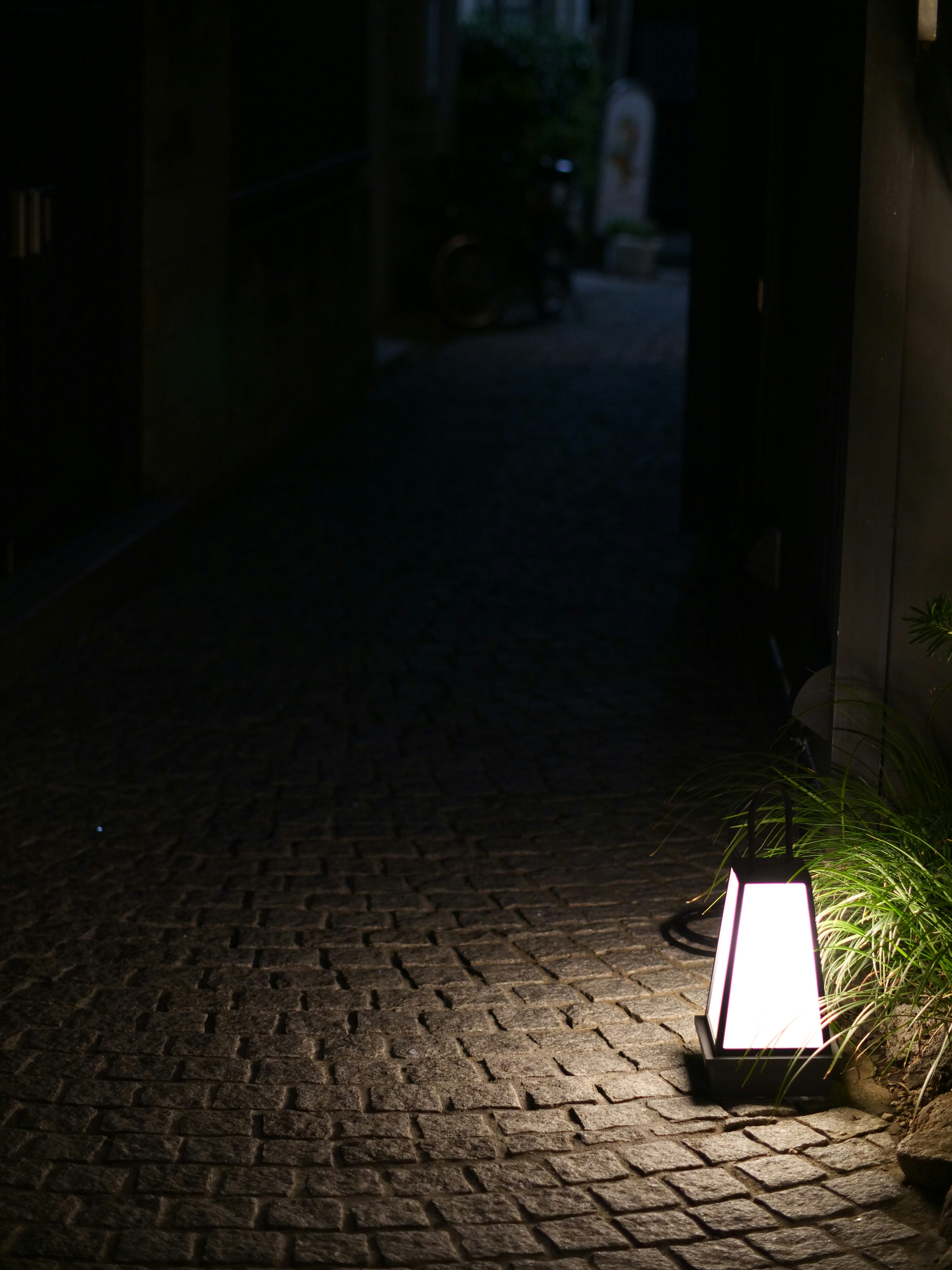 Eine Laterne beleuchtet einen Kopfsteinpflasterweg in einer dunklen Gasse