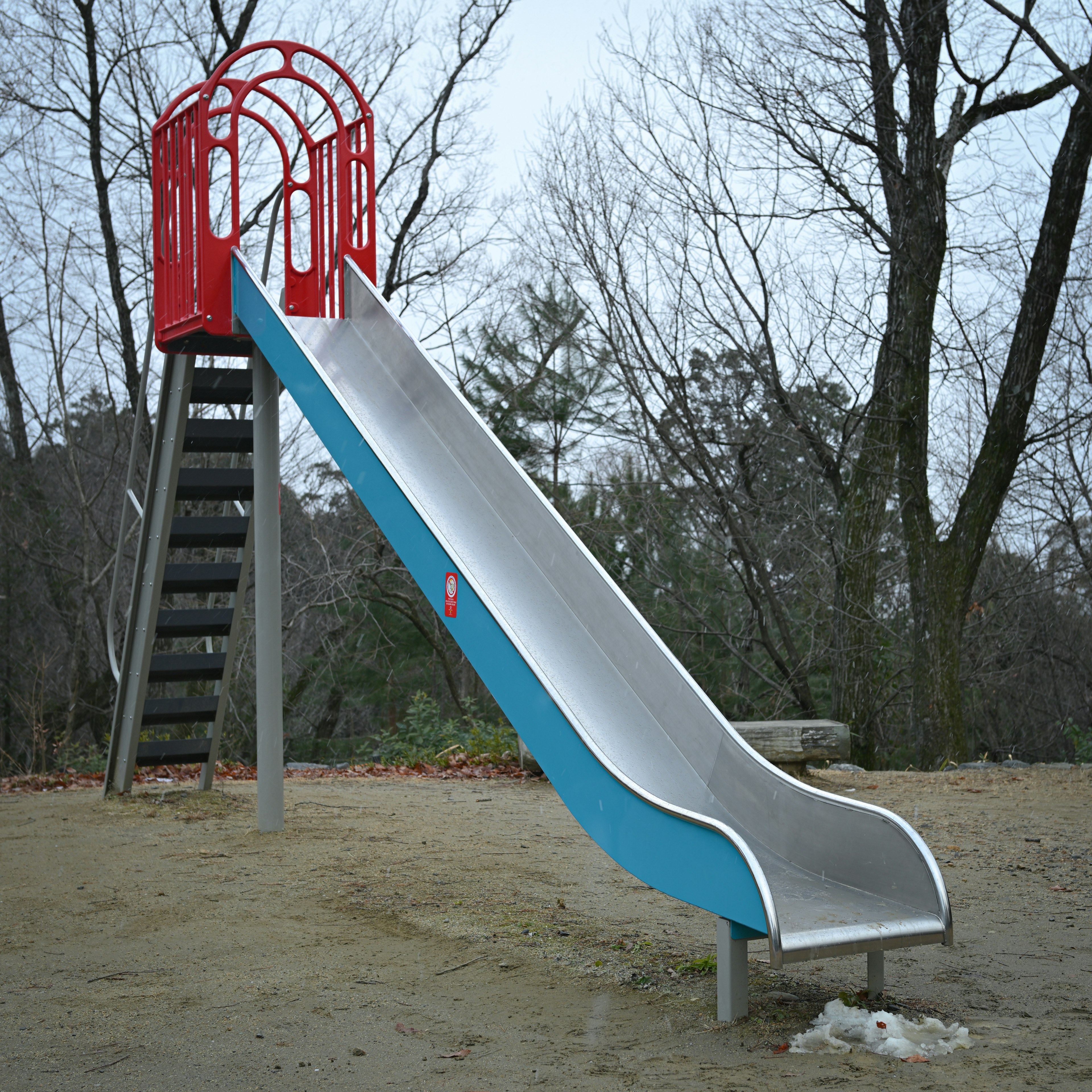 Playground slide with red handrails and blue sliding surface metal stairs