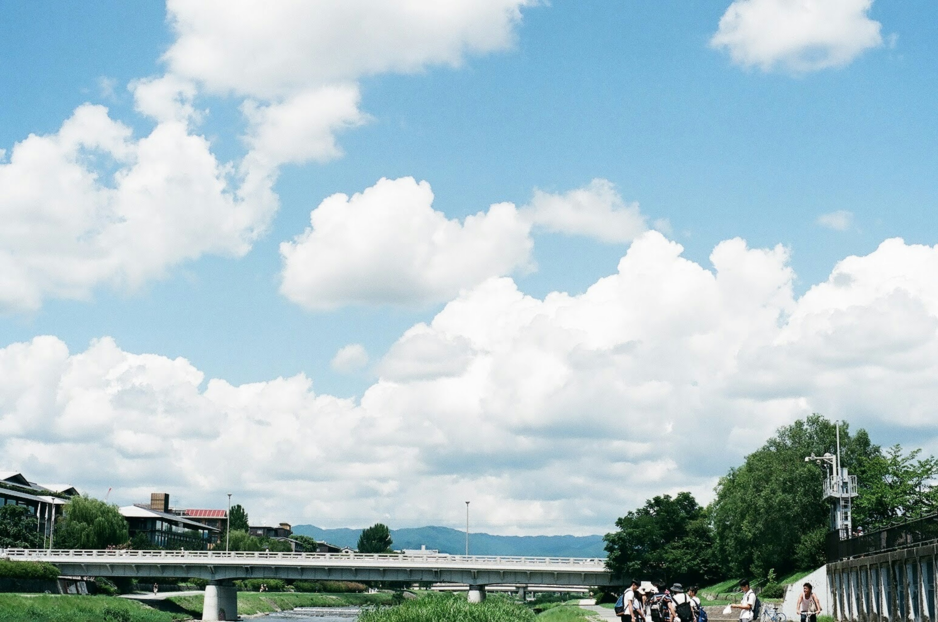 Vista escénica junto al río con cielo azul y nubes blancas mostrando personas paseando