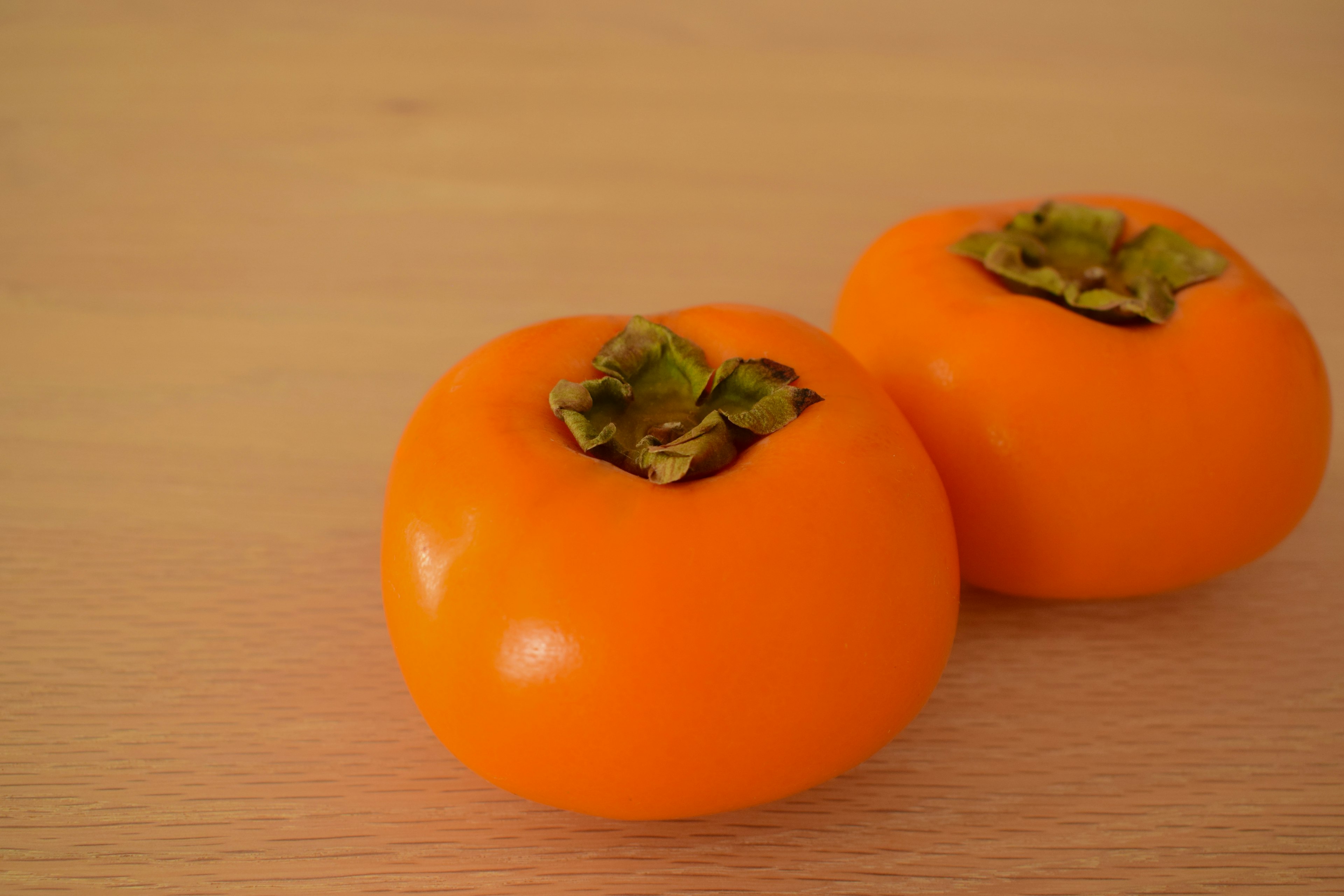 Two orange persimmons placed on a wooden table