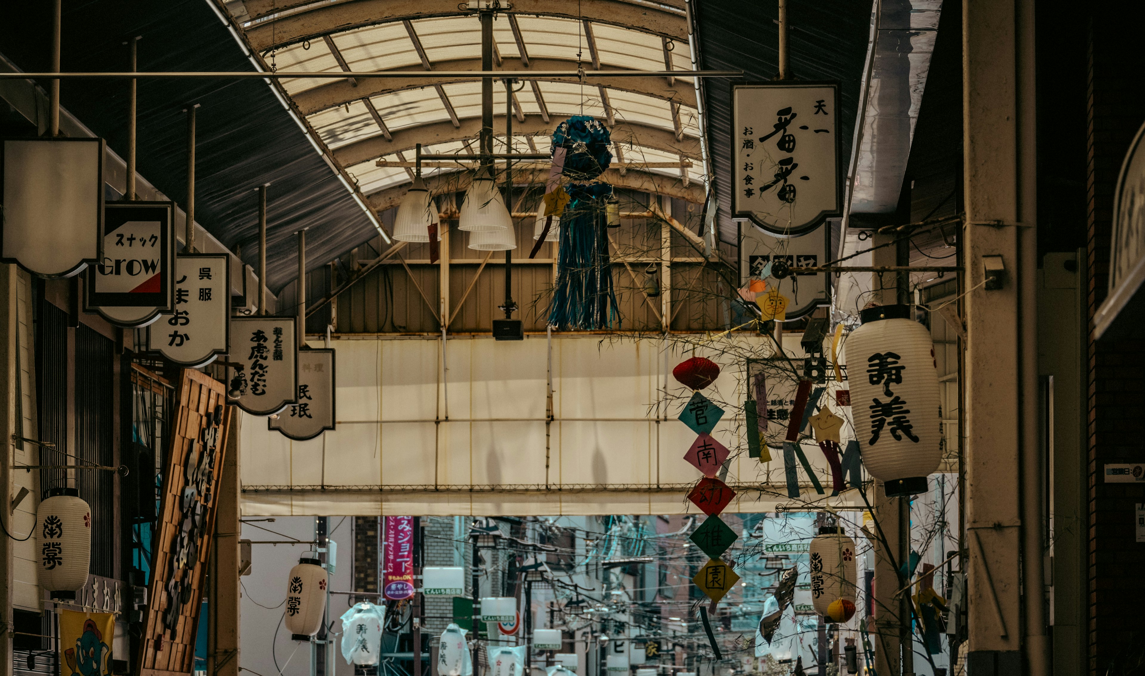 商店街の屋根の下に吊るされた提灯と色とりどりの装飾がある風景