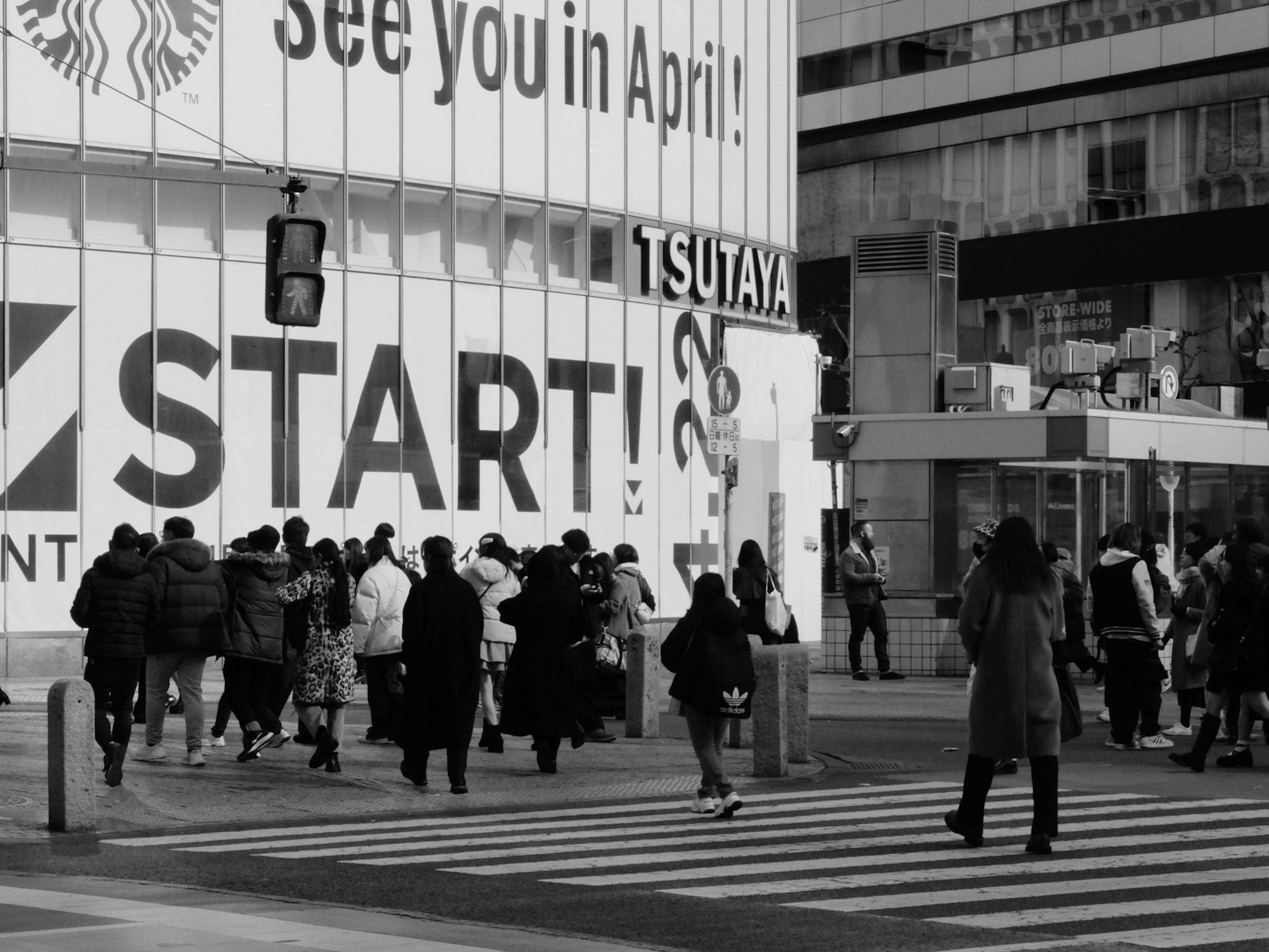 사람들이 TSUTAYA 간판과 START 텍스트가 있는 흑백 도시 풍경에서 길을 건너고 있습니다