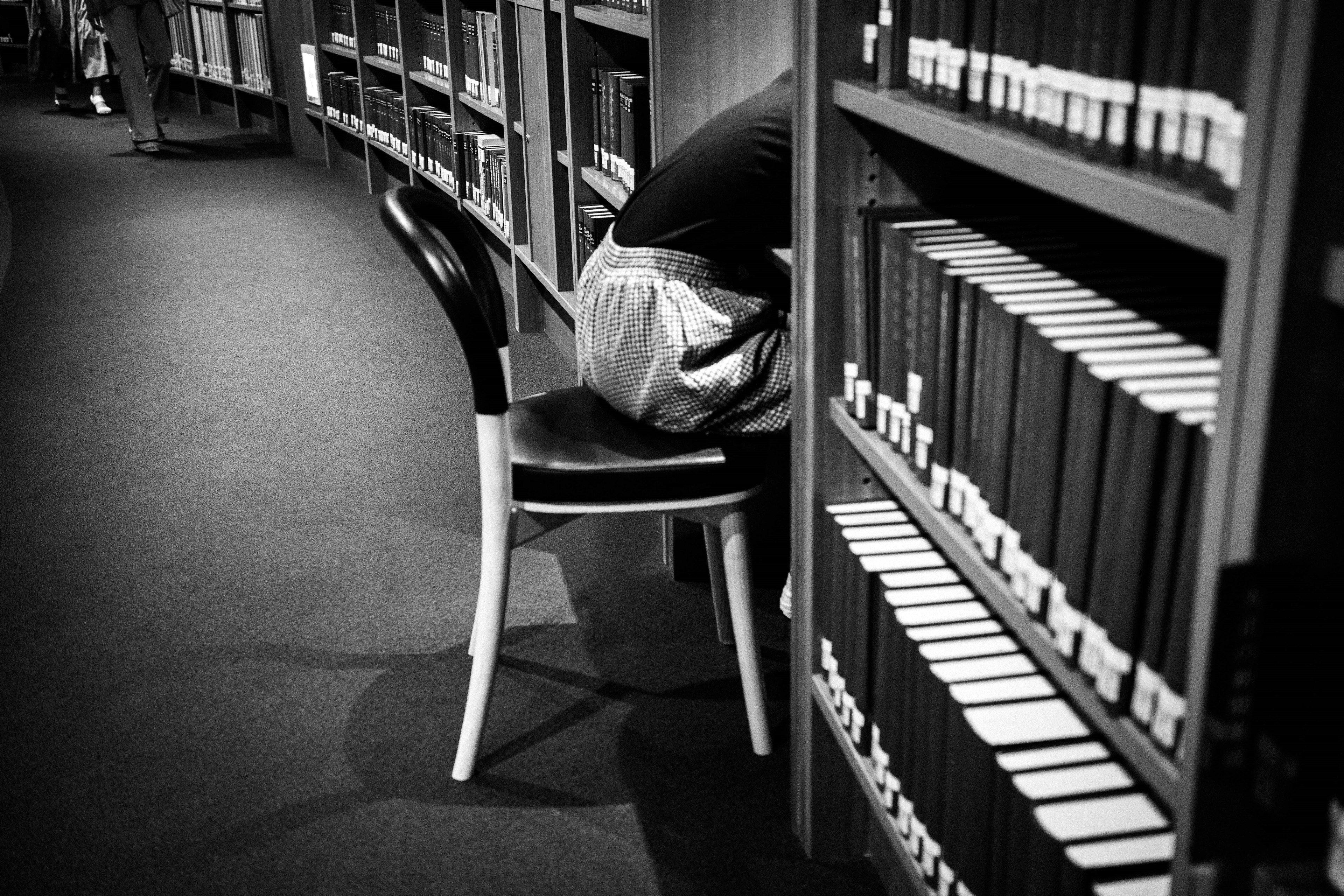 Eine Person sitzt mit dem Rücken zur Kamera in einer Bibliothek zwischen Bücherregalen