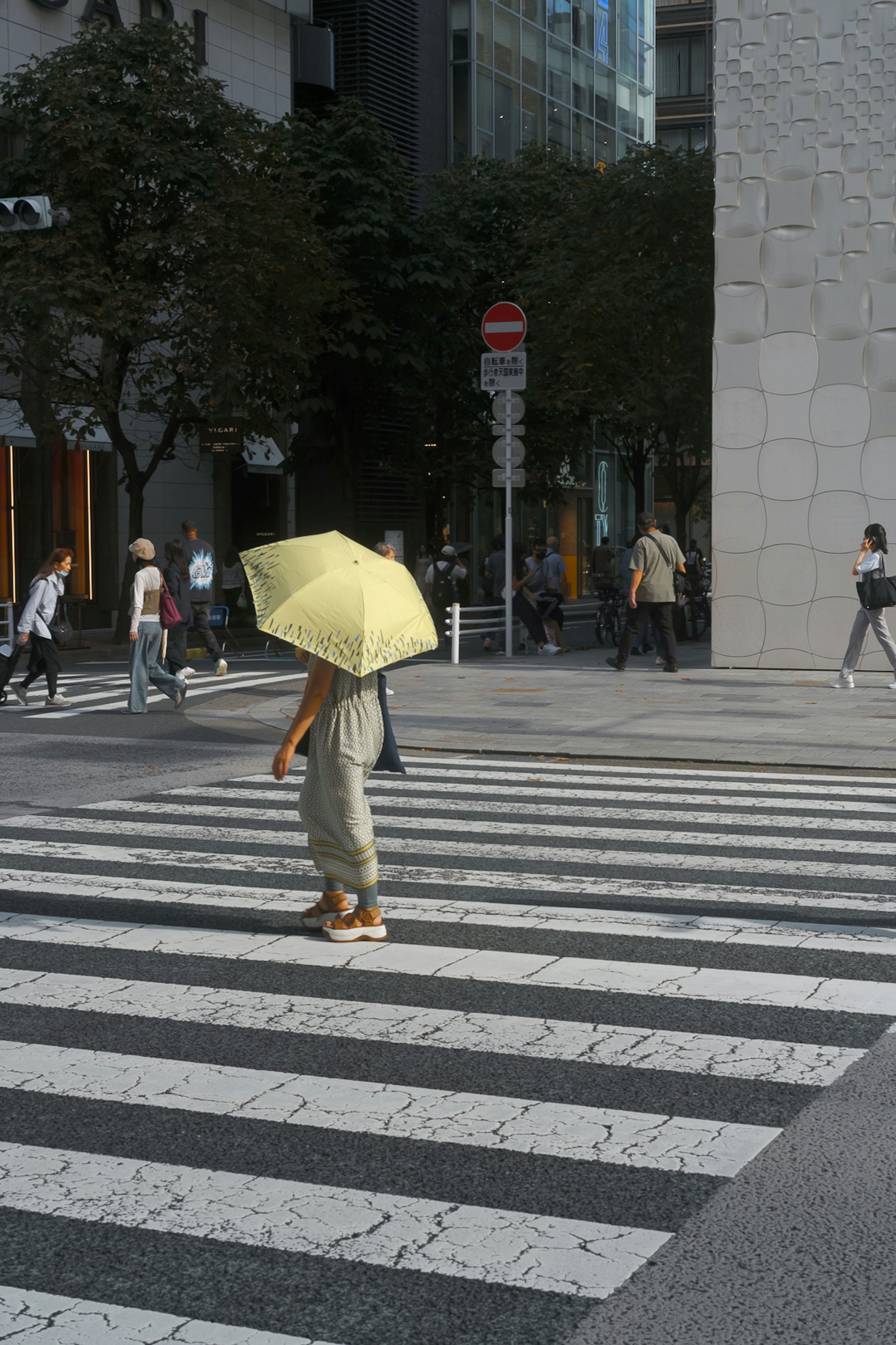 黄色い傘を持つ人が横断歩道を渡っている都会の風景