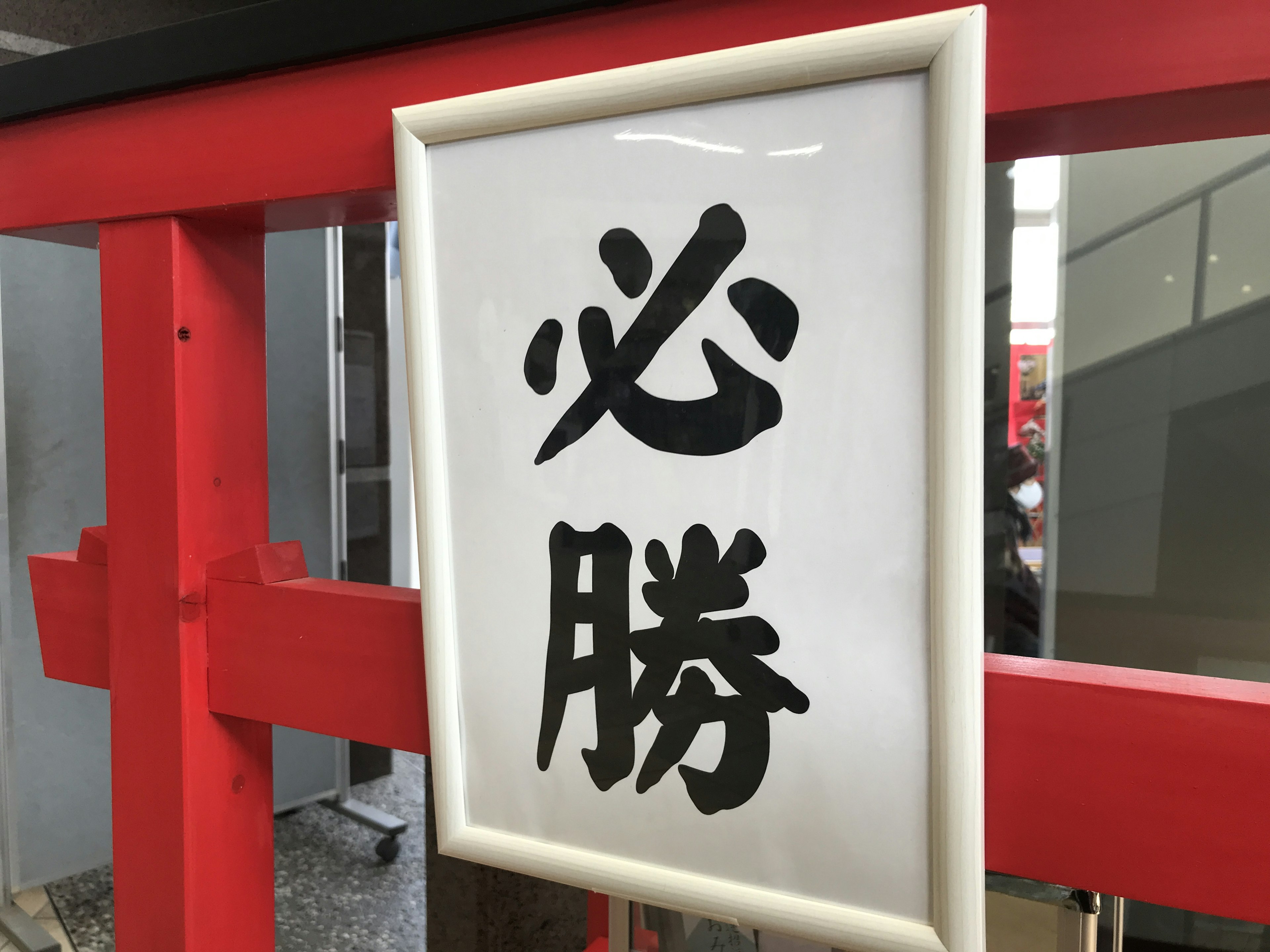 A white sign with the kanji '必勝' near a red torii gate