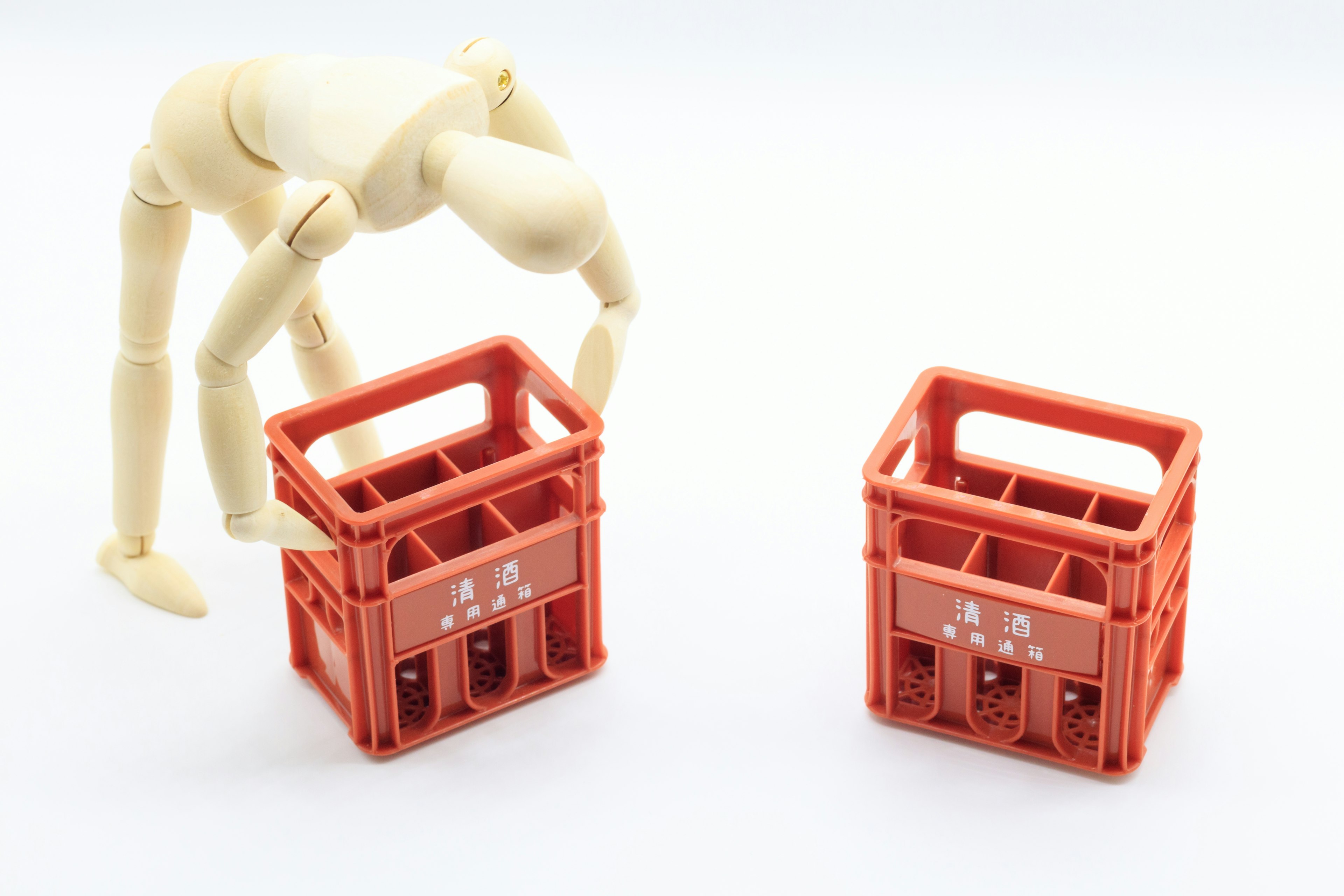 Wooden mannequin reaching for red plastic crates on a white background