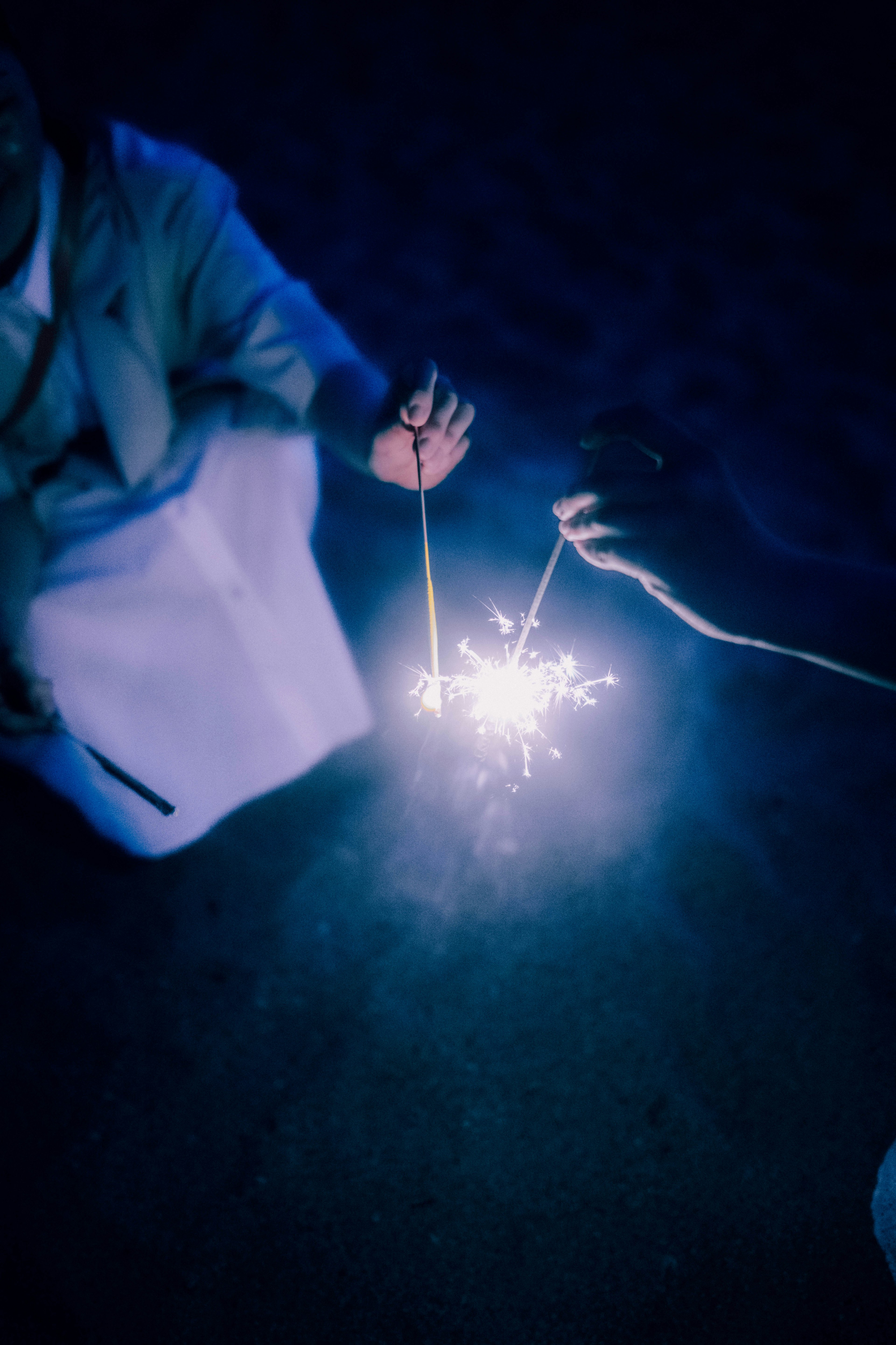 Two hands holding sparklers against a dark background