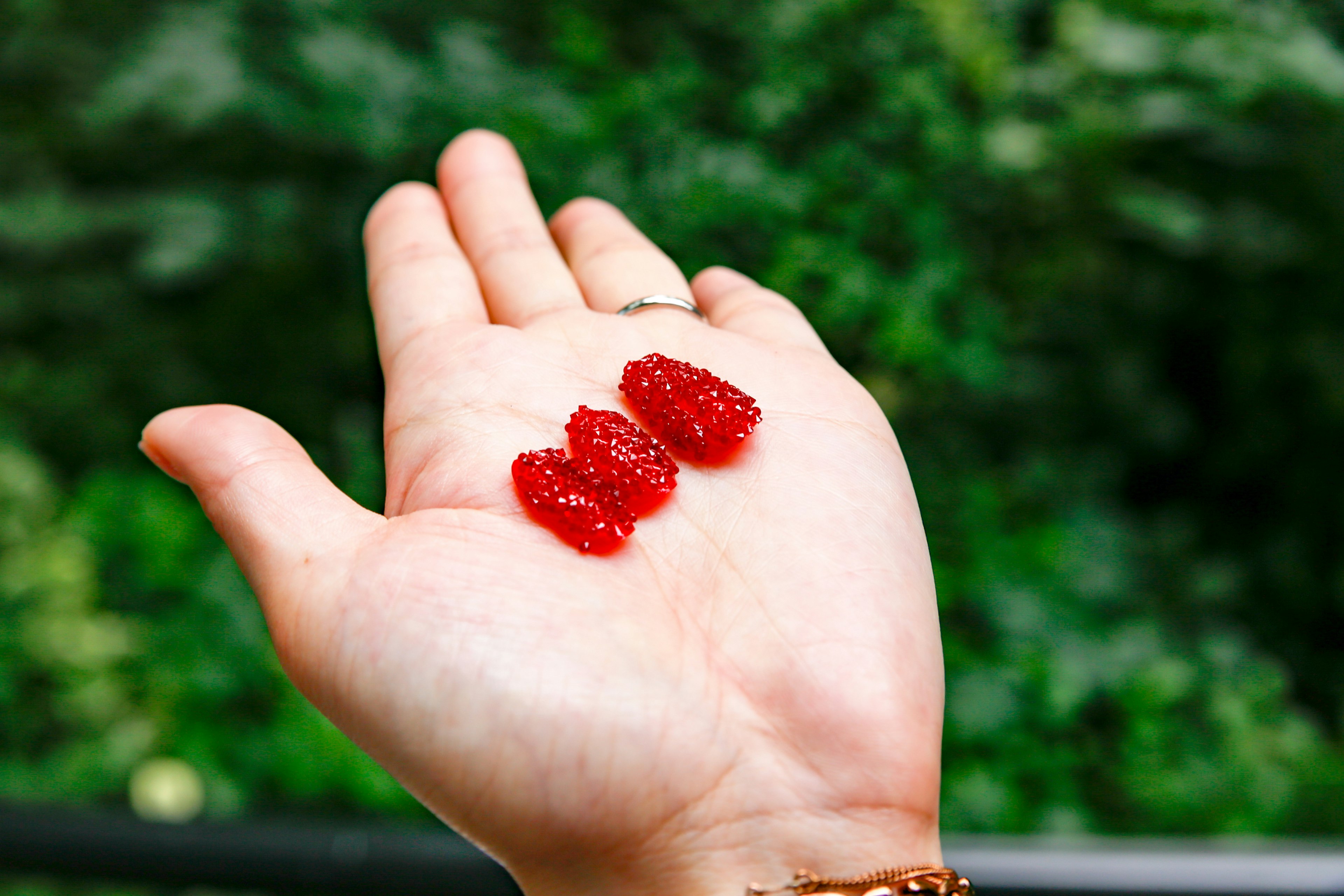 Mano che tiene tre caramelle rosse simili a gelatina all'aperto