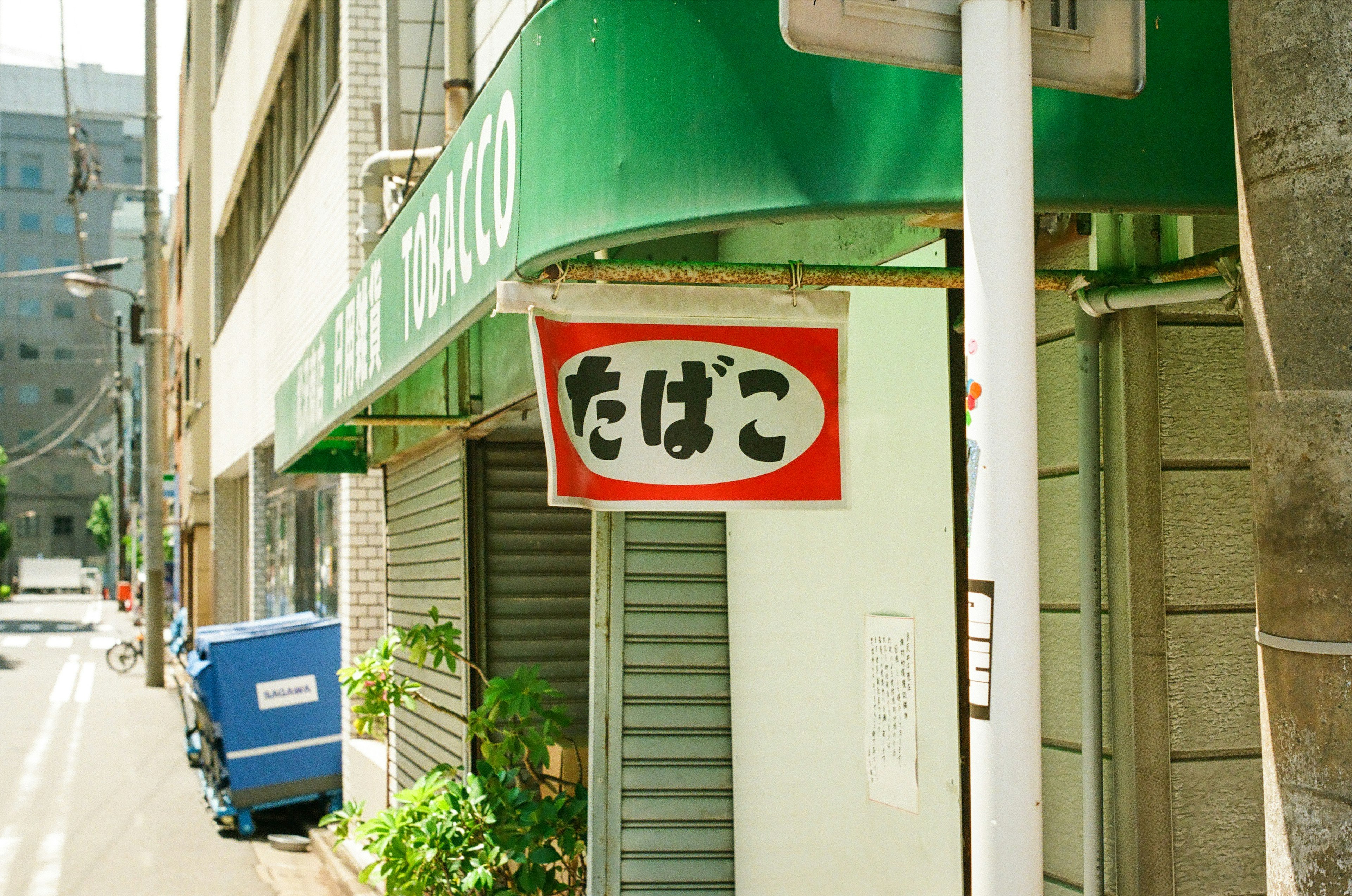 Cartel rojo con la palabra 'たばこ' frente a un edificio con toldo verde