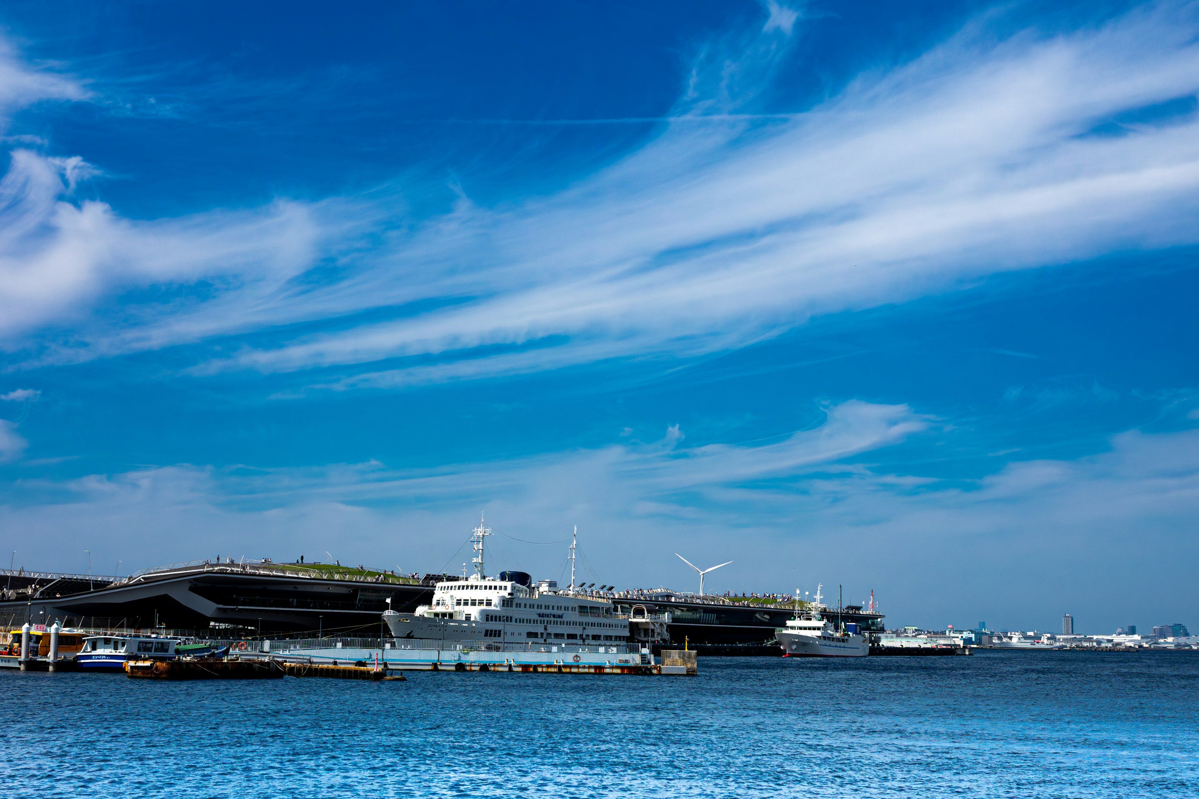 Escena de puerto con barcos y edificios bajo un cielo azul y nubes