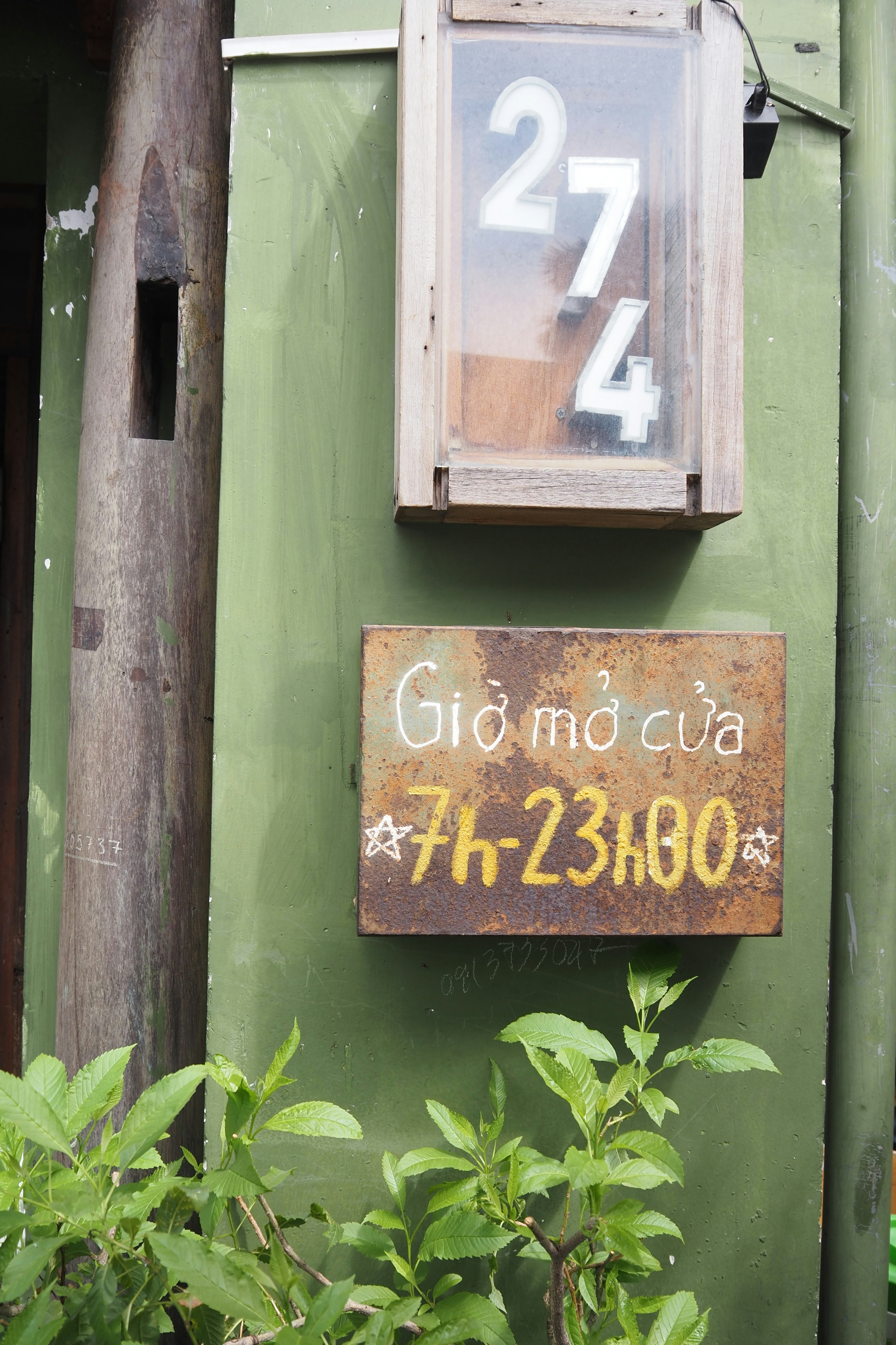 Wooden sign on green wall displaying number 274 and opening hours from 7 to 23 80