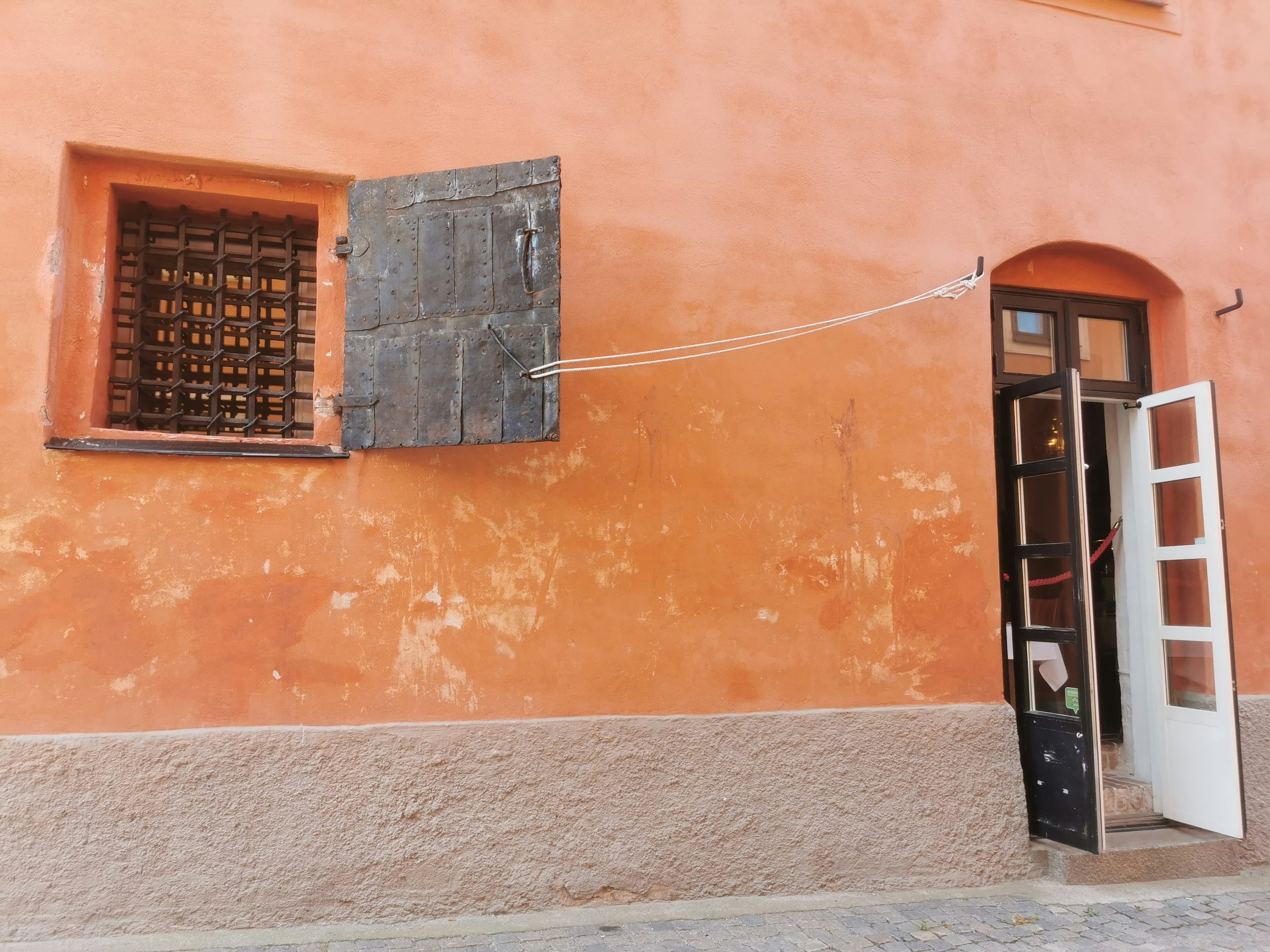 Exterior of a building with an orange wall featuring a wooden window and an open door