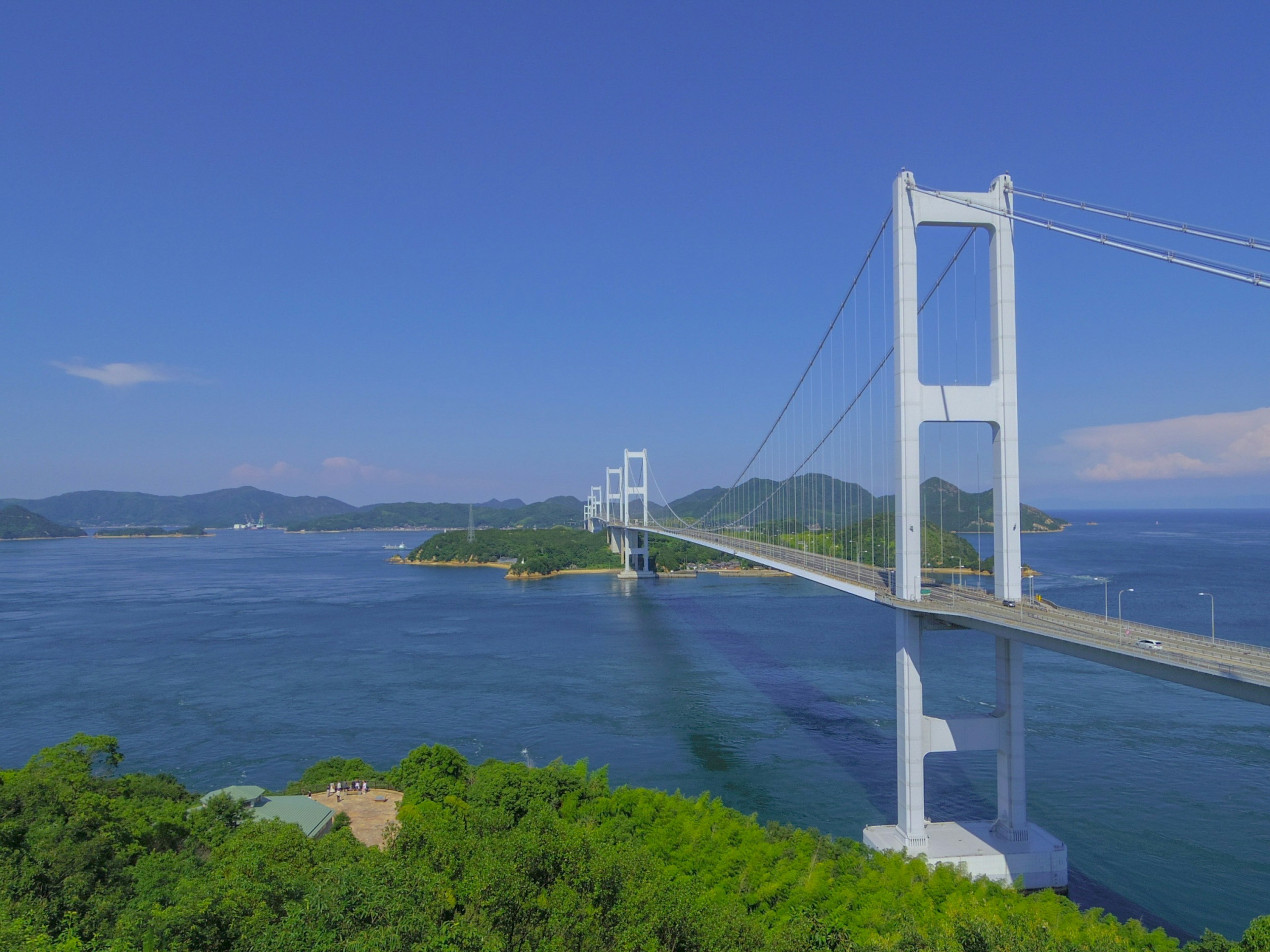 Eine weiße Hängebrücke, die über blaues Wasser unter einem klaren Himmel spannt