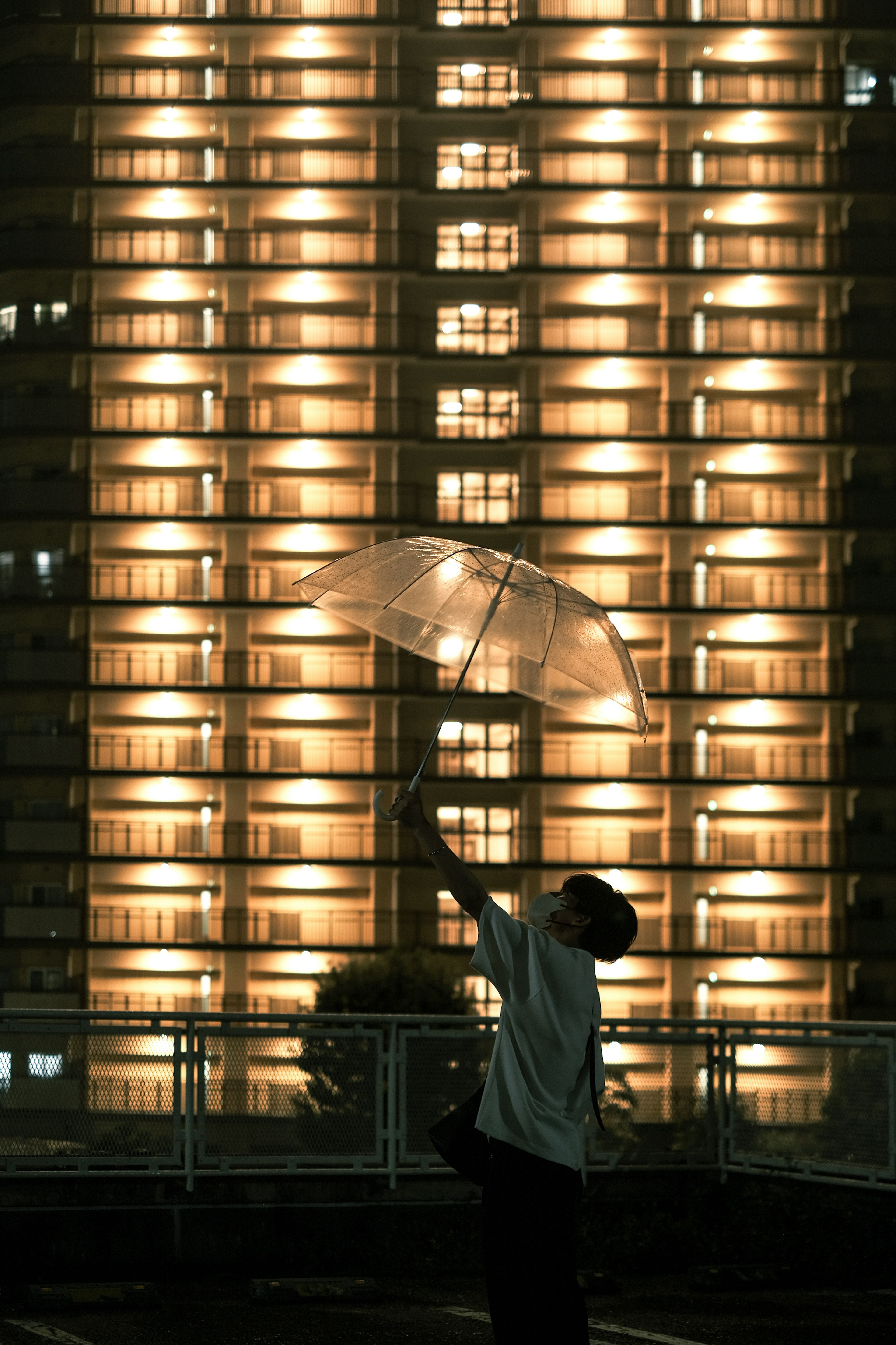 A person holding an umbrella stands in front of a brightly lit building at night