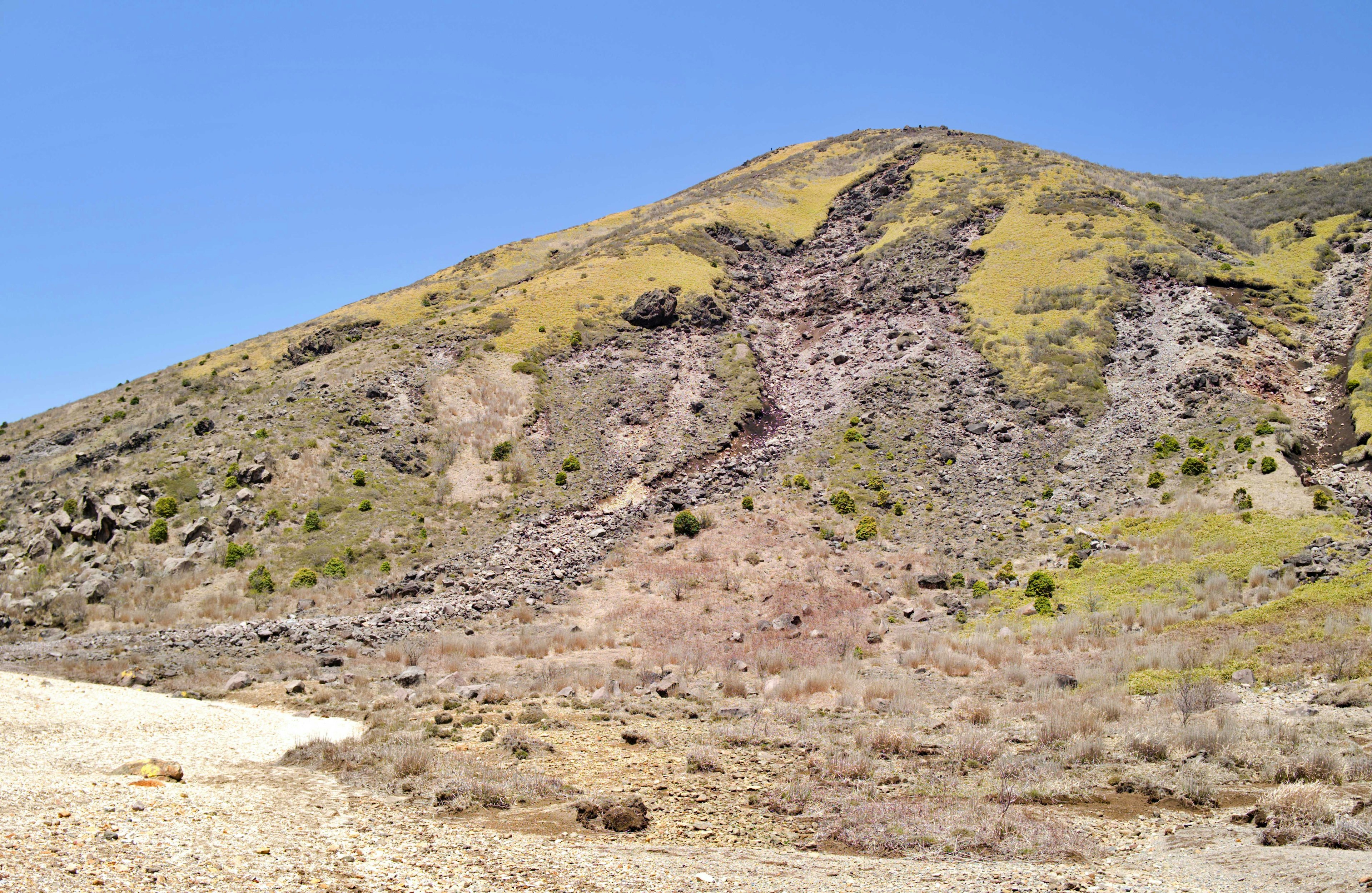 Dry mountain slope with green grass and rock layers