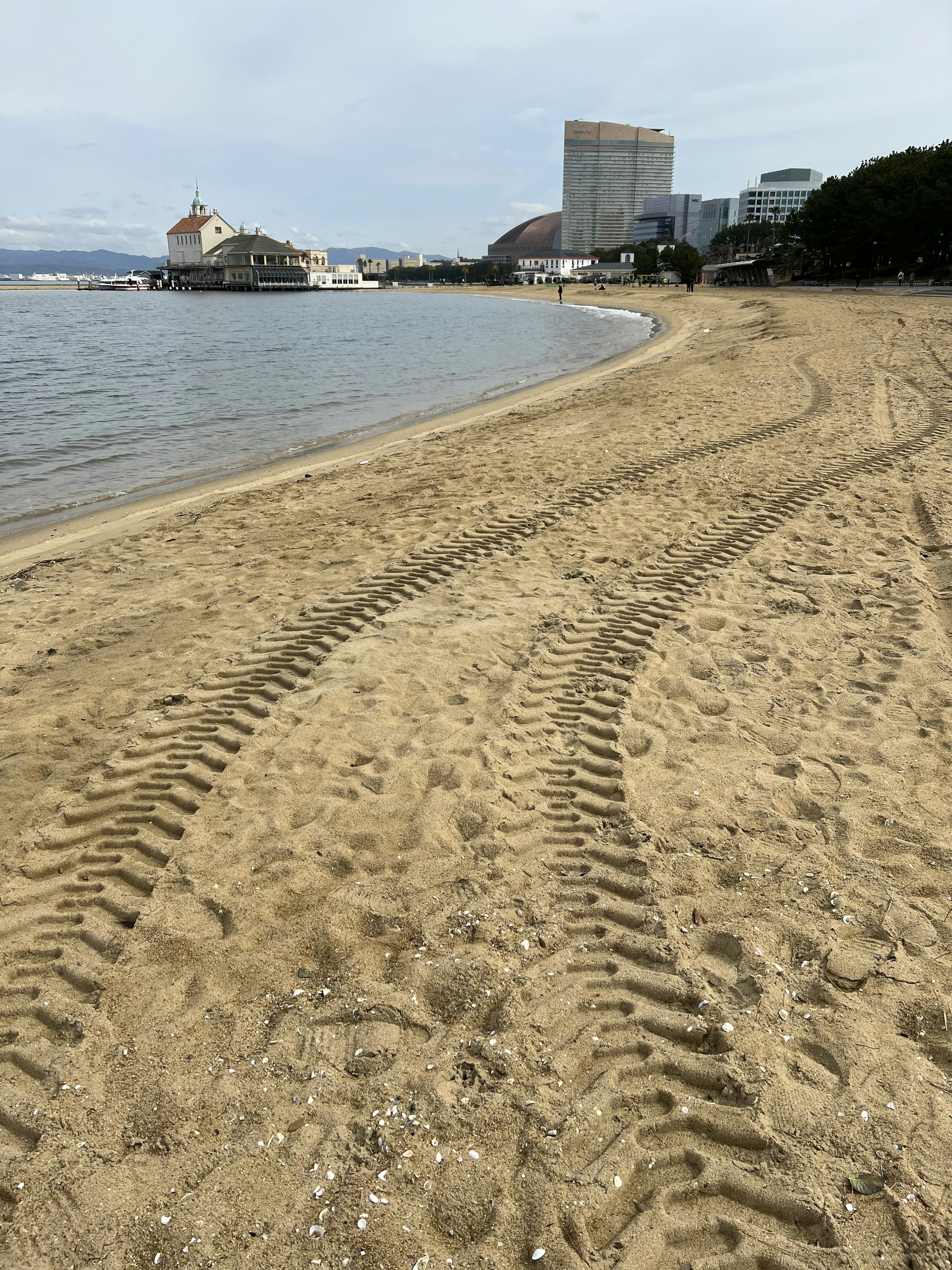 Jejak ban di pantai berpasir dengan laut tenang di latar belakang