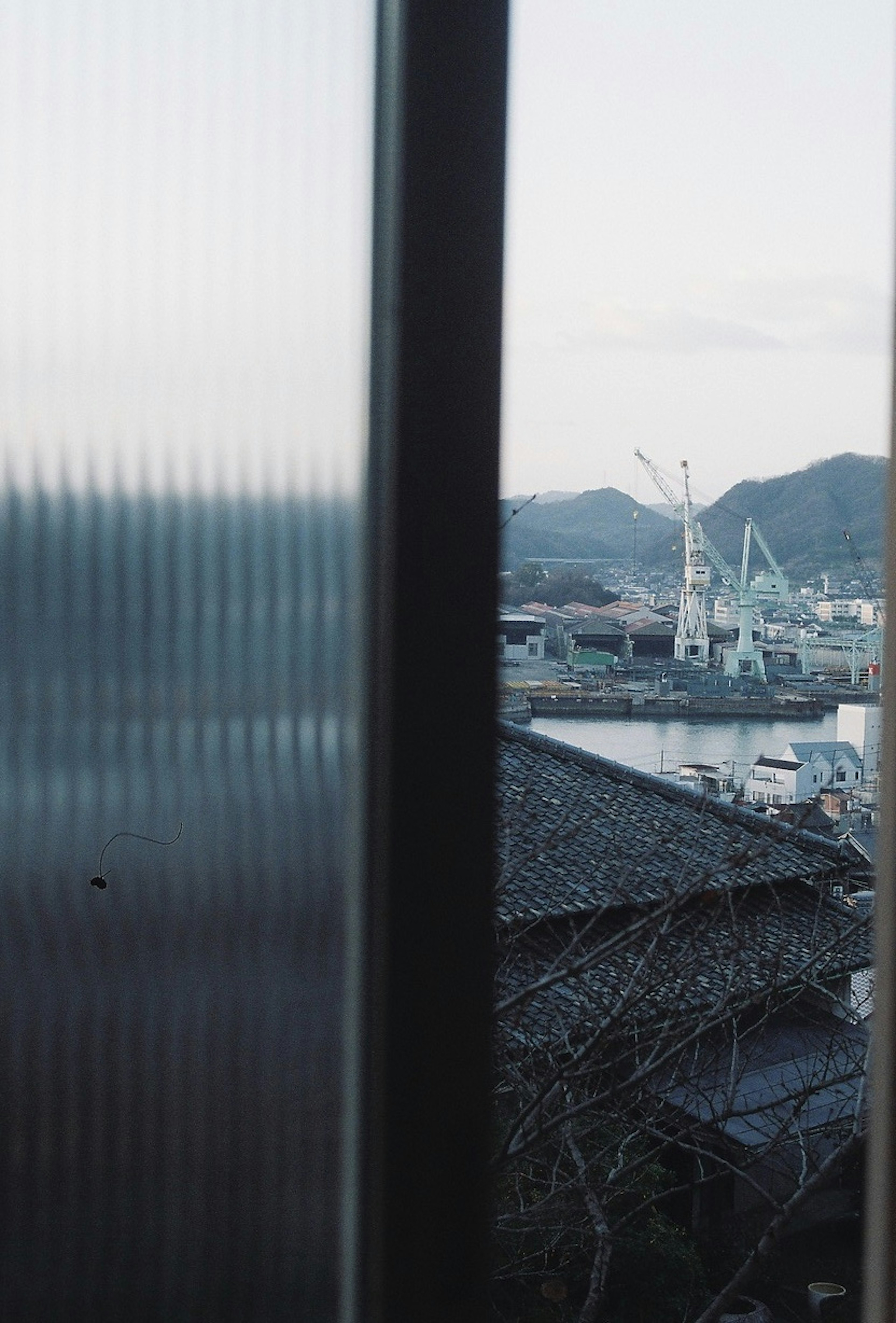 View of a port with cranes and mountains in the background through a window