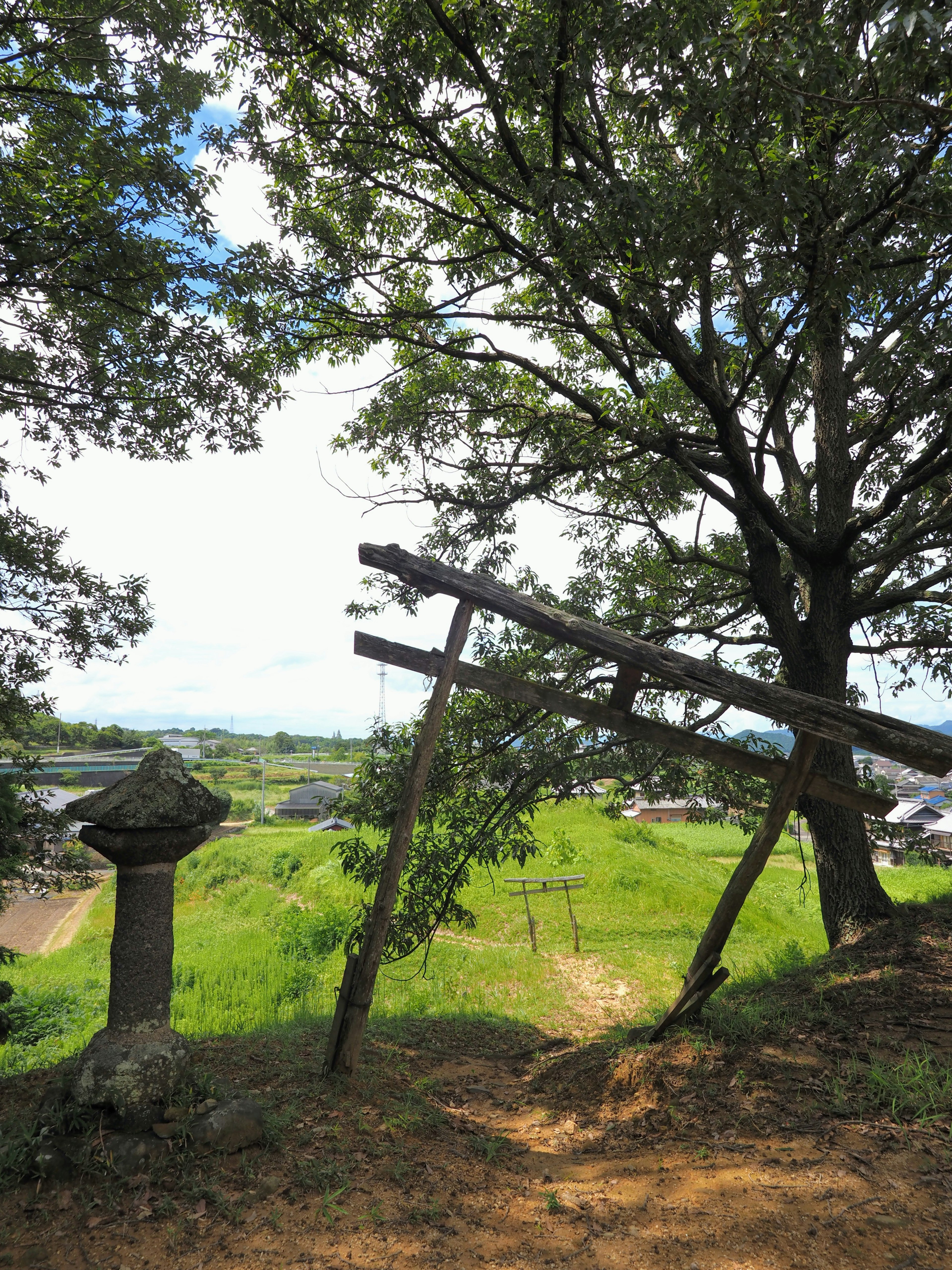 青々とした草原と木々の景色に傾いた木製の構造物がある風景