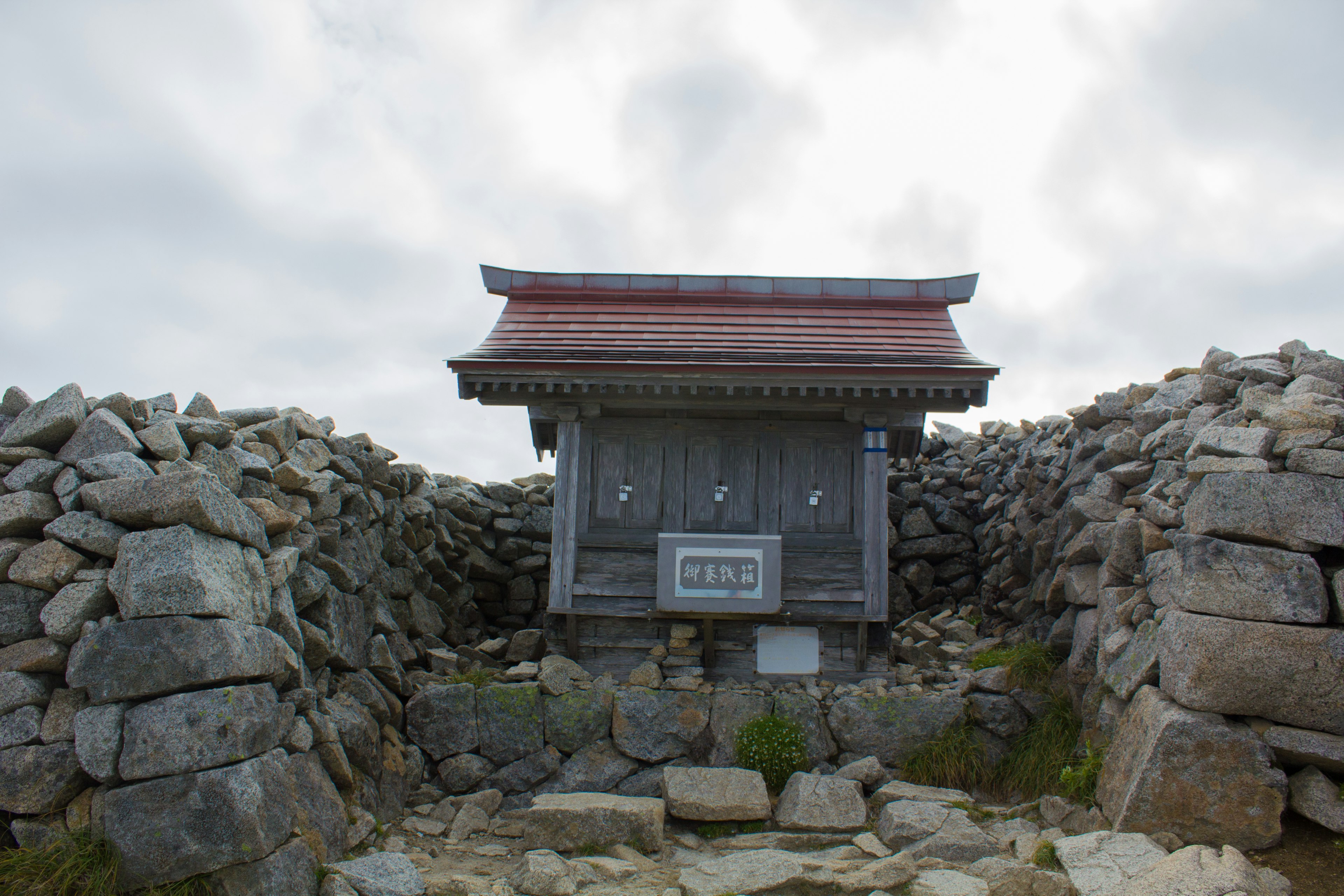 一座小型神社建筑被石头环绕，天空多云