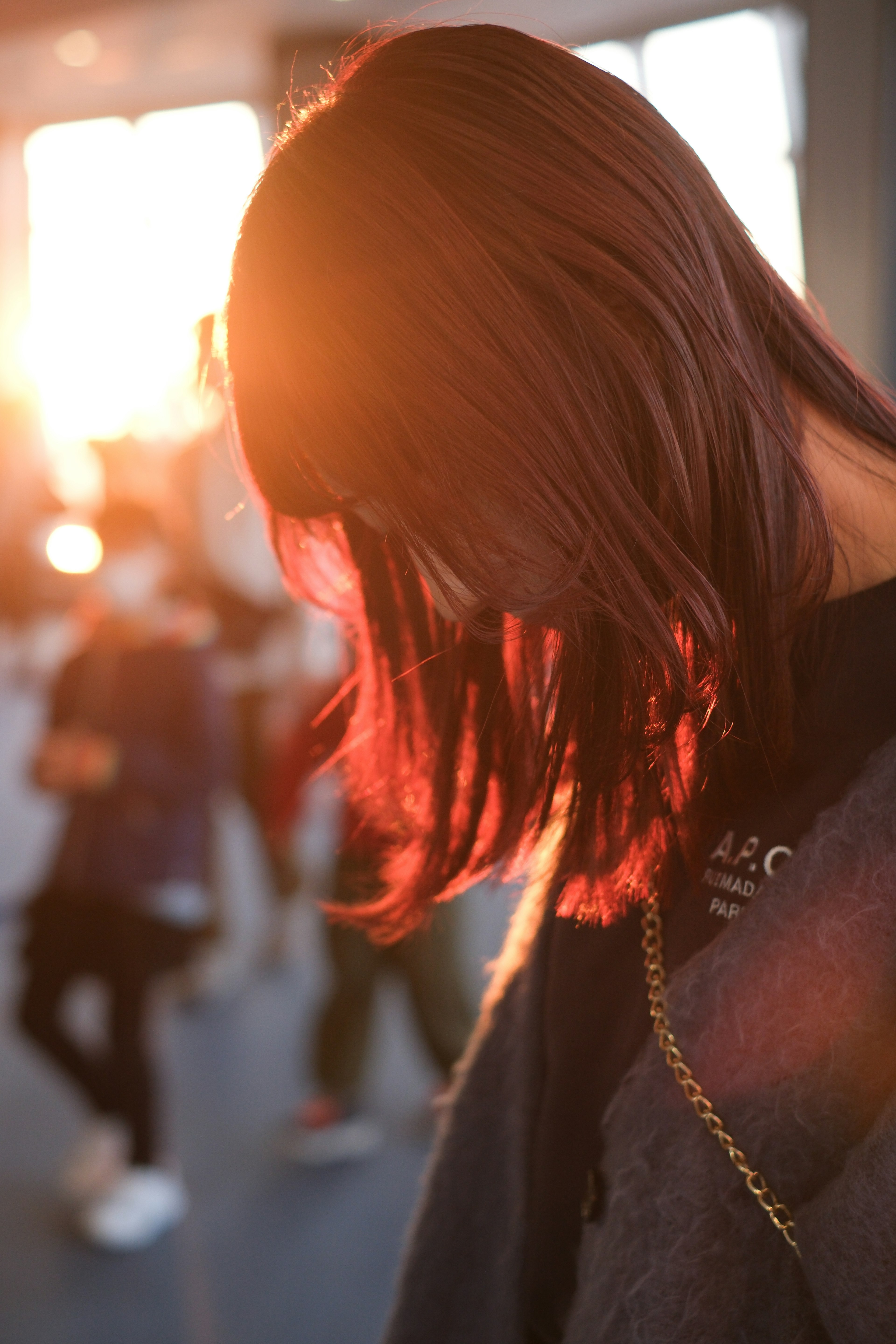 Silhouette d'une femme avec de longs cheveux à la lumière du coucher de soleil entourée de personnes floues