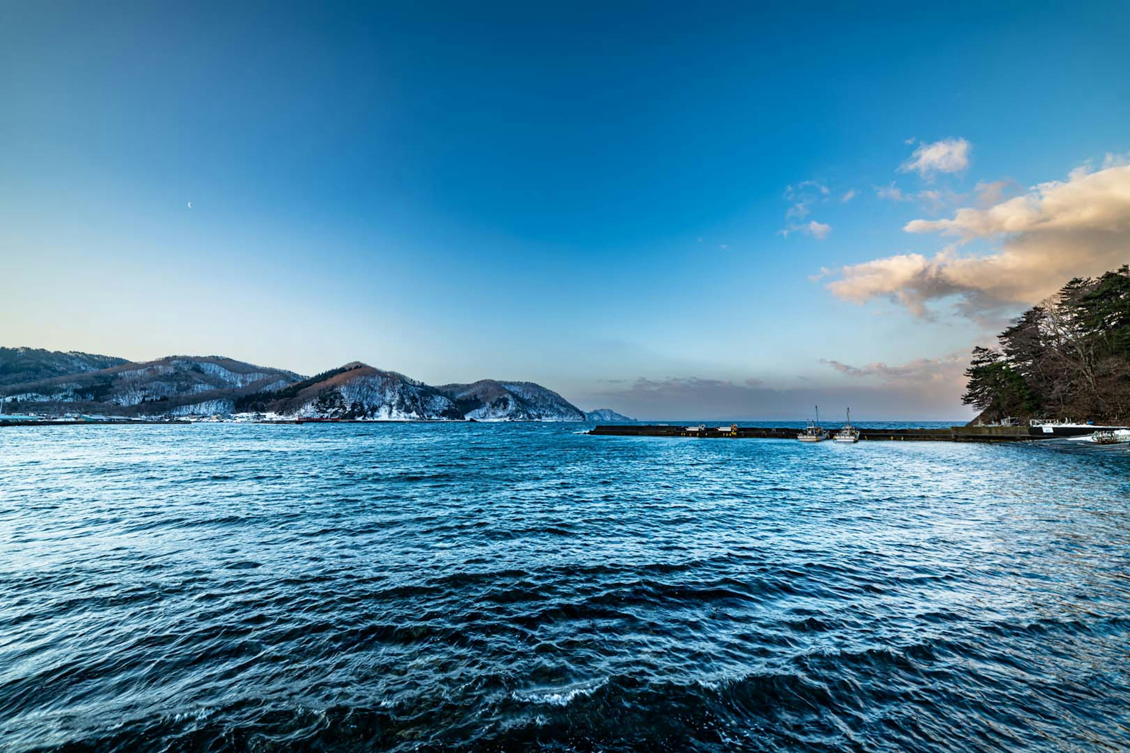 Pemandangan laut biru dan pegunungan di bawah langit cerah