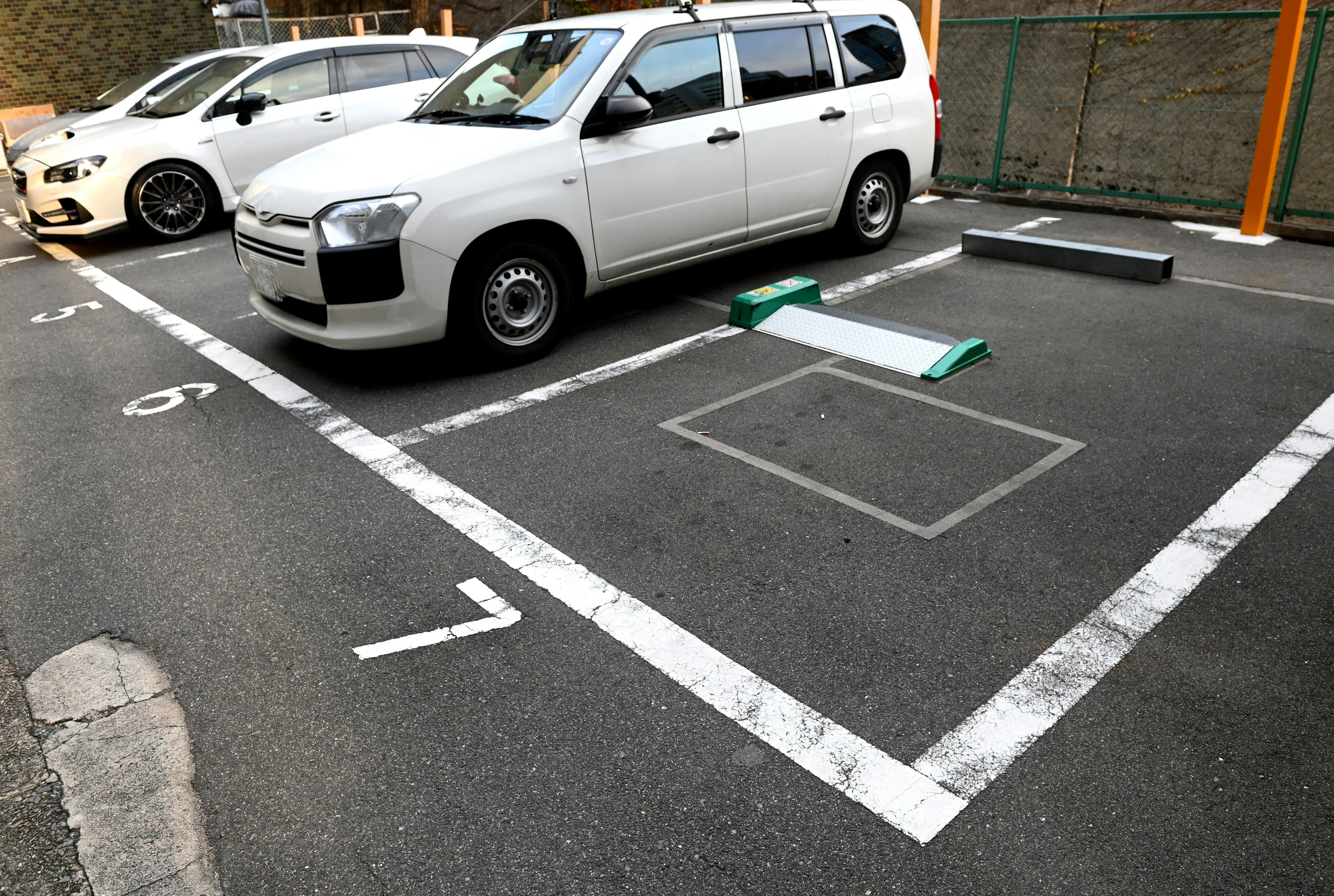 A parking lot featuring a white car parked next to an empty parking space outlined in white lines