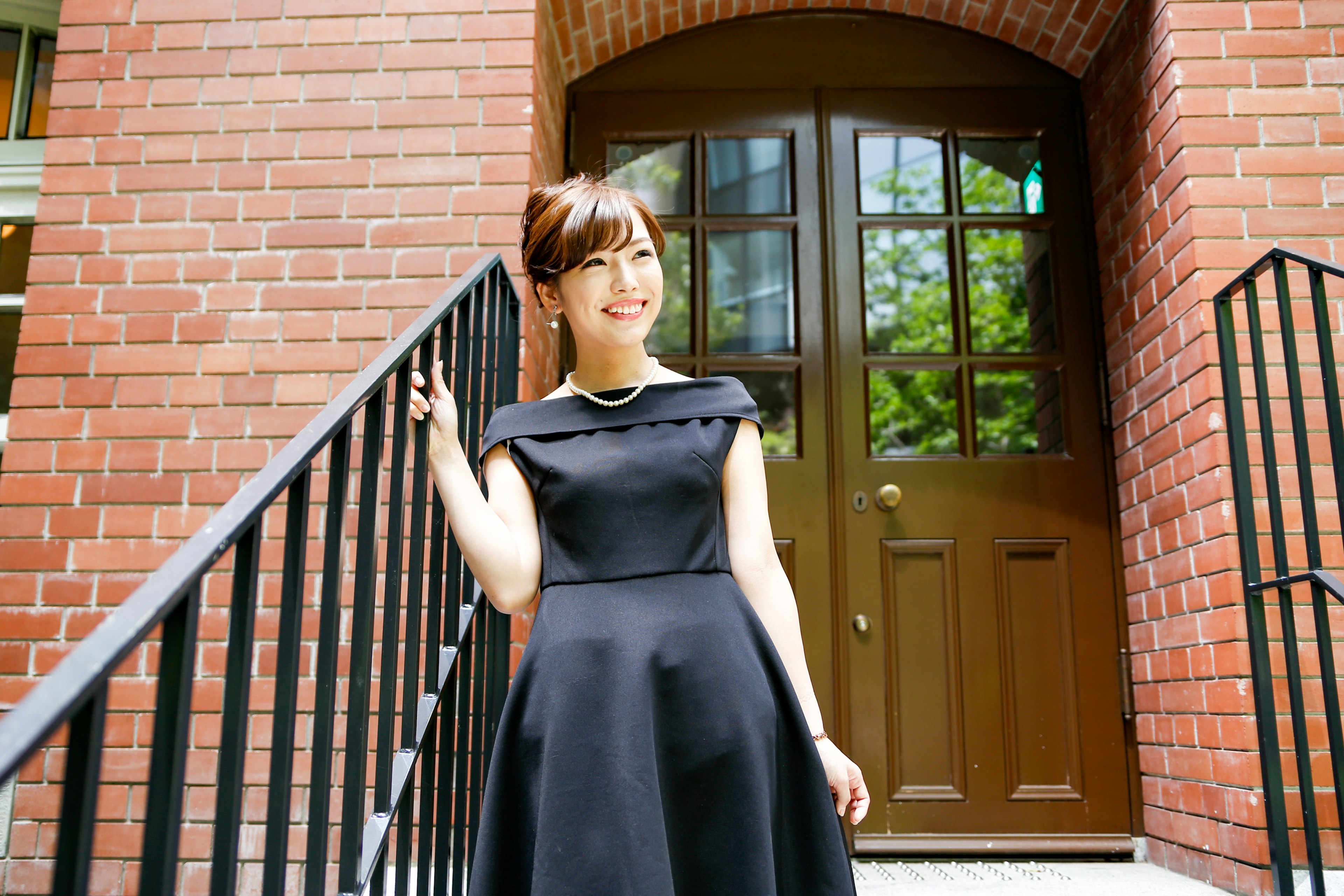 A woman in a black dress standing on the stairs of a brick building