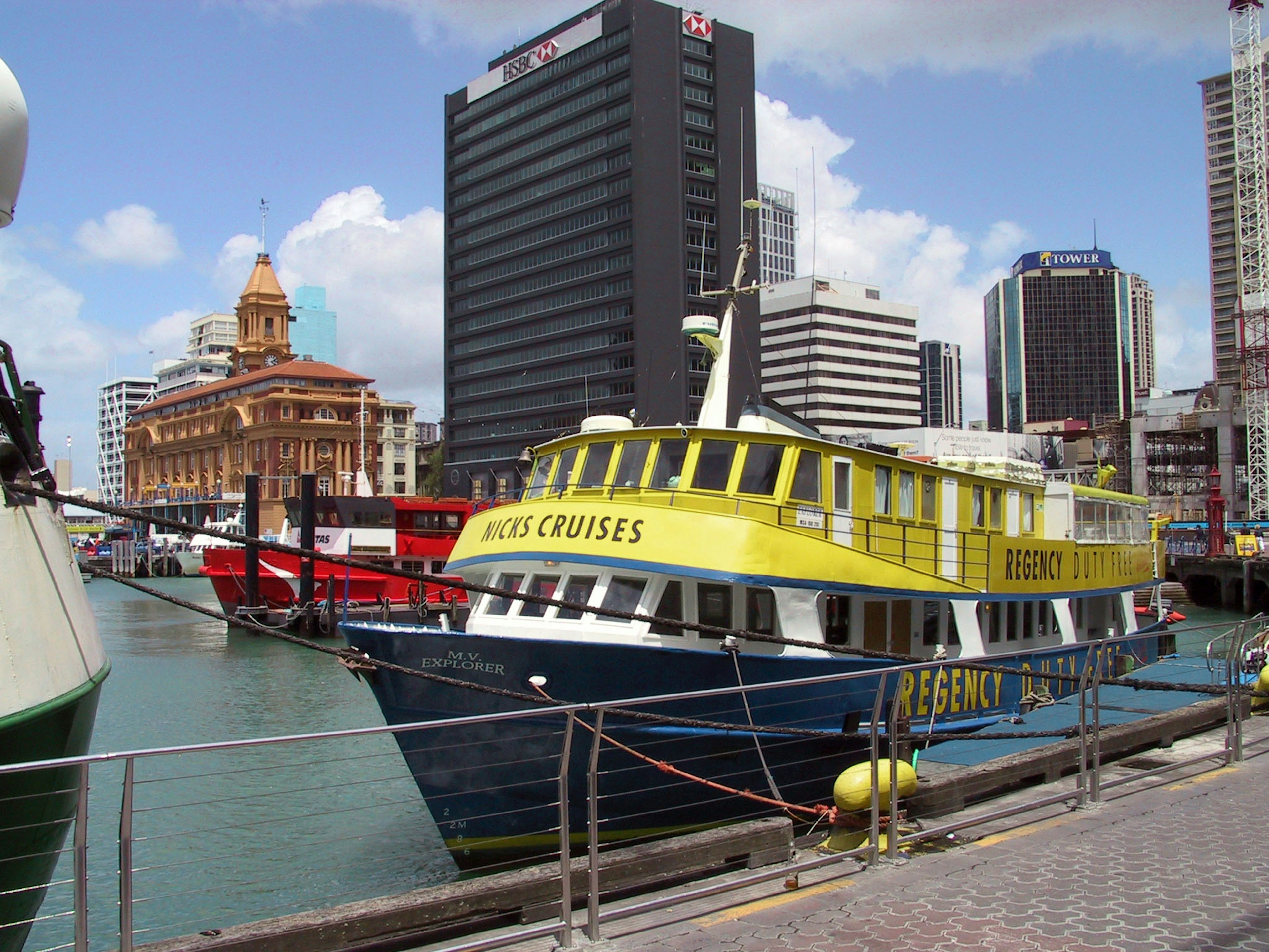 A blue and yellow boat docked at a harbor with skyscrapers and historical buildings in the background