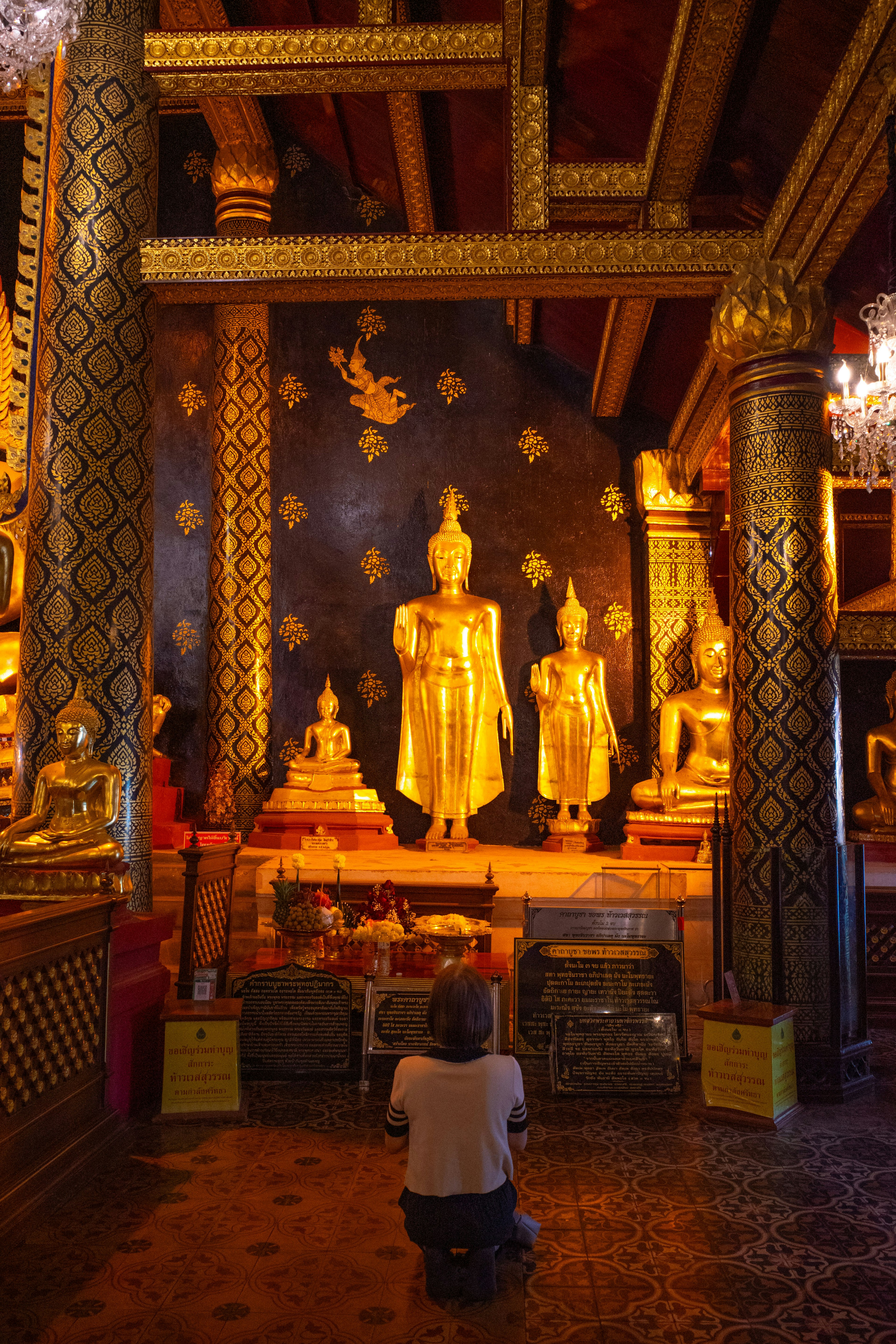 Interior of a temple featuring golden Buddha statues and a person praying in front