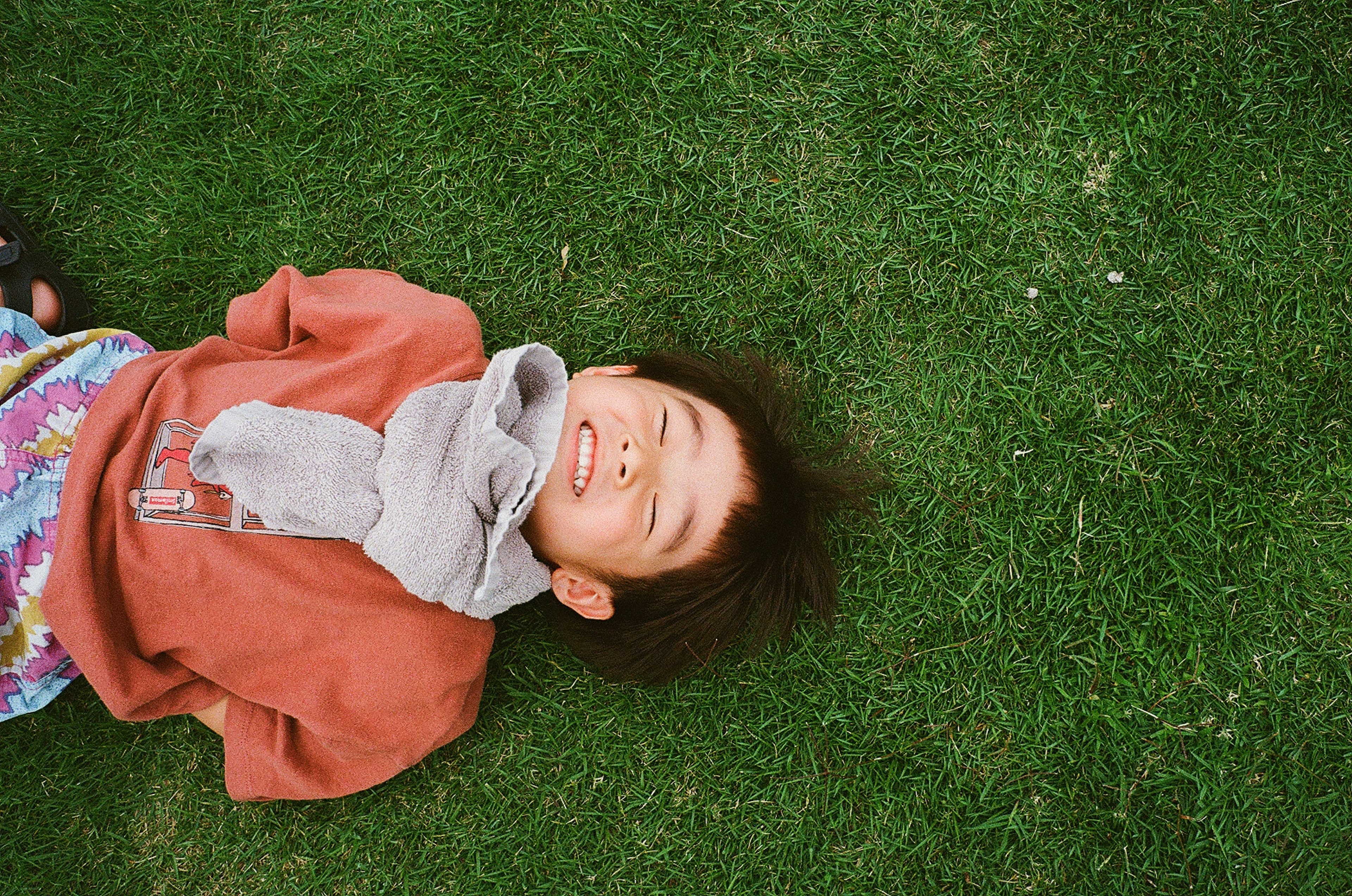 笑顔で芝生の上に寝転ぶ子供の写真