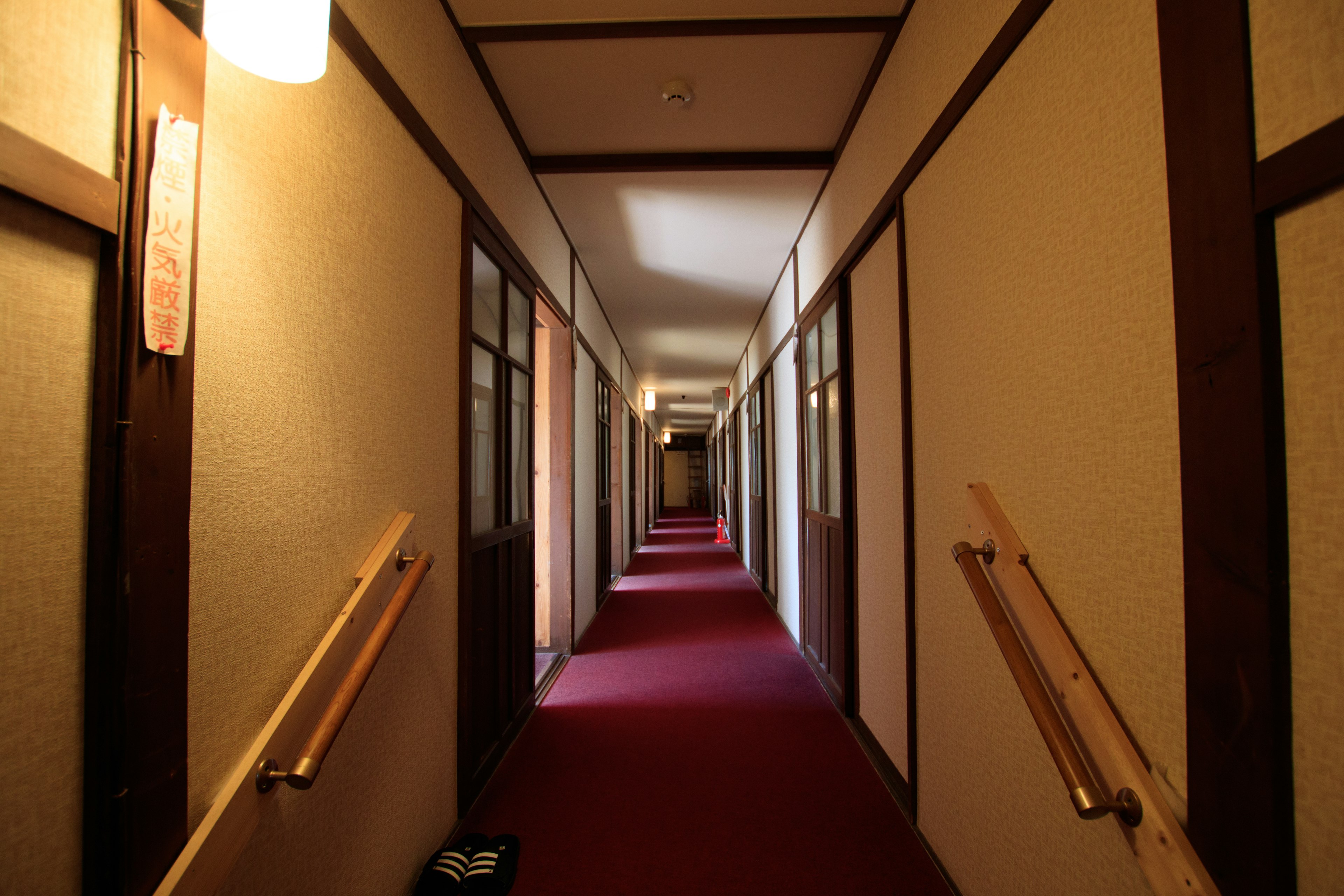 Interior of a Japanese inn featuring a long corridor with red carpet and wooden handrails