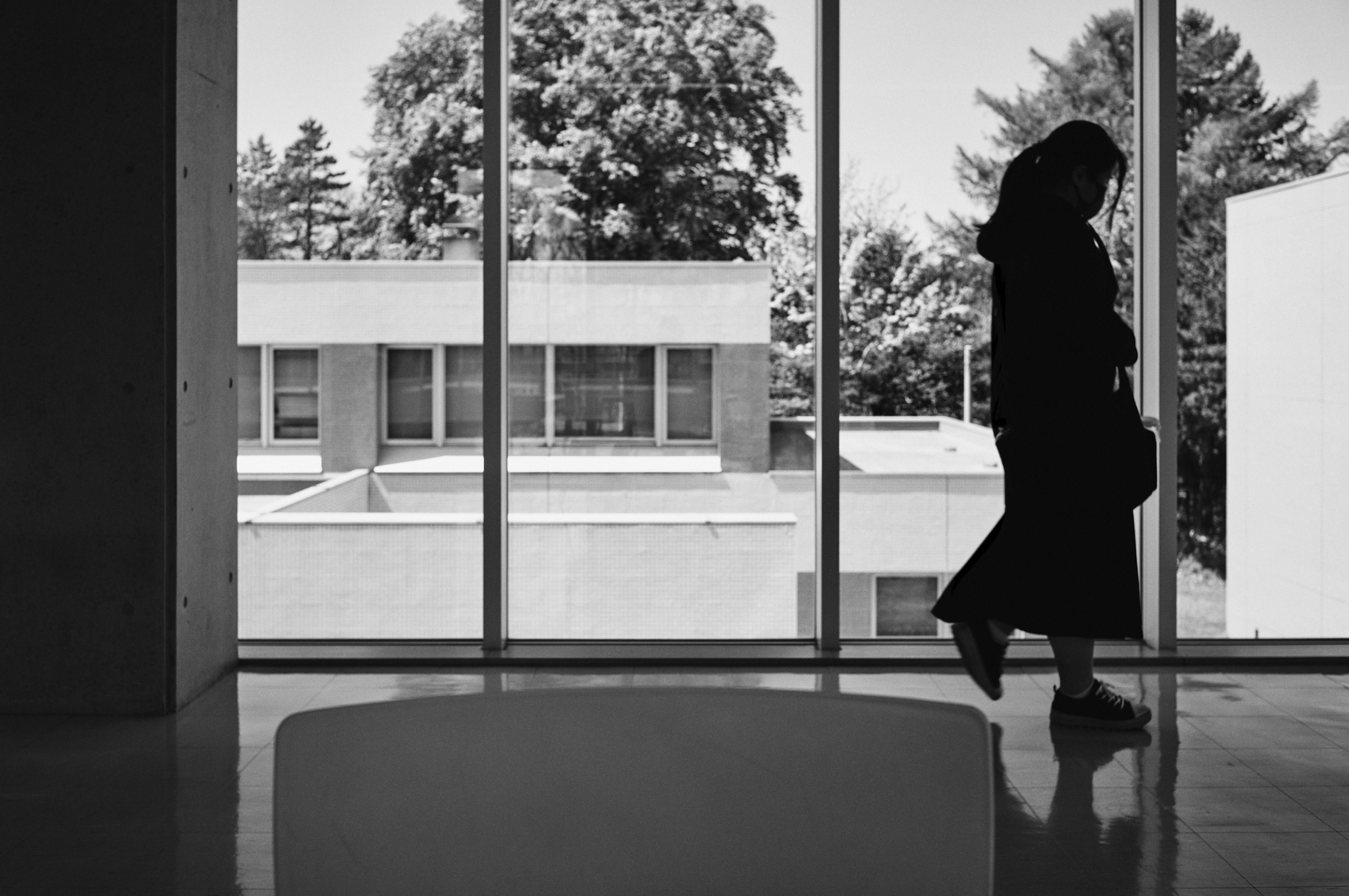 Silhouette di una donna che cammina vicino a una finestra con architettura moderna sullo sfondo