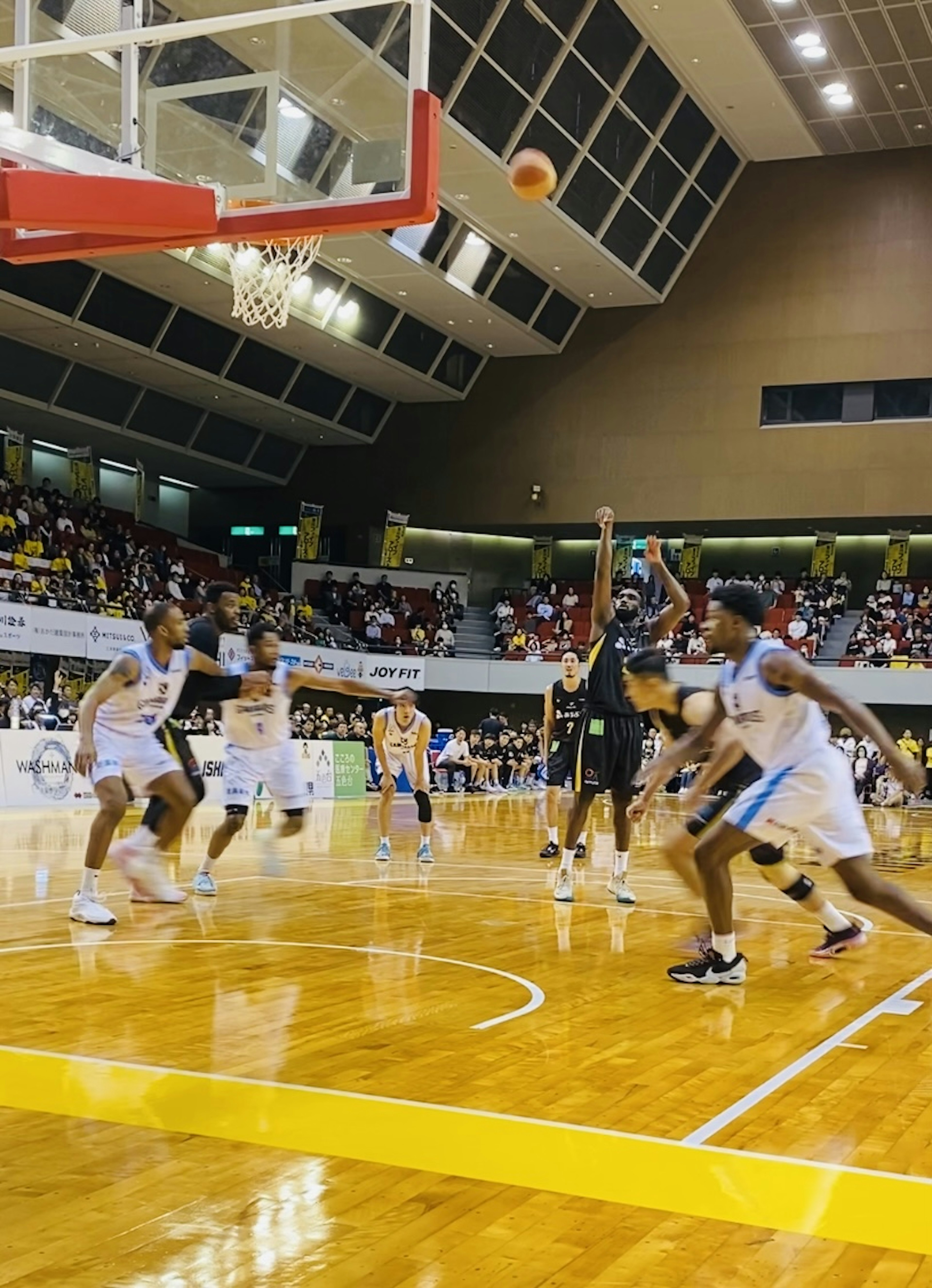 Pertandingan basket dengan pemain yang melakukan tembakan sementara penonton menyaksikan