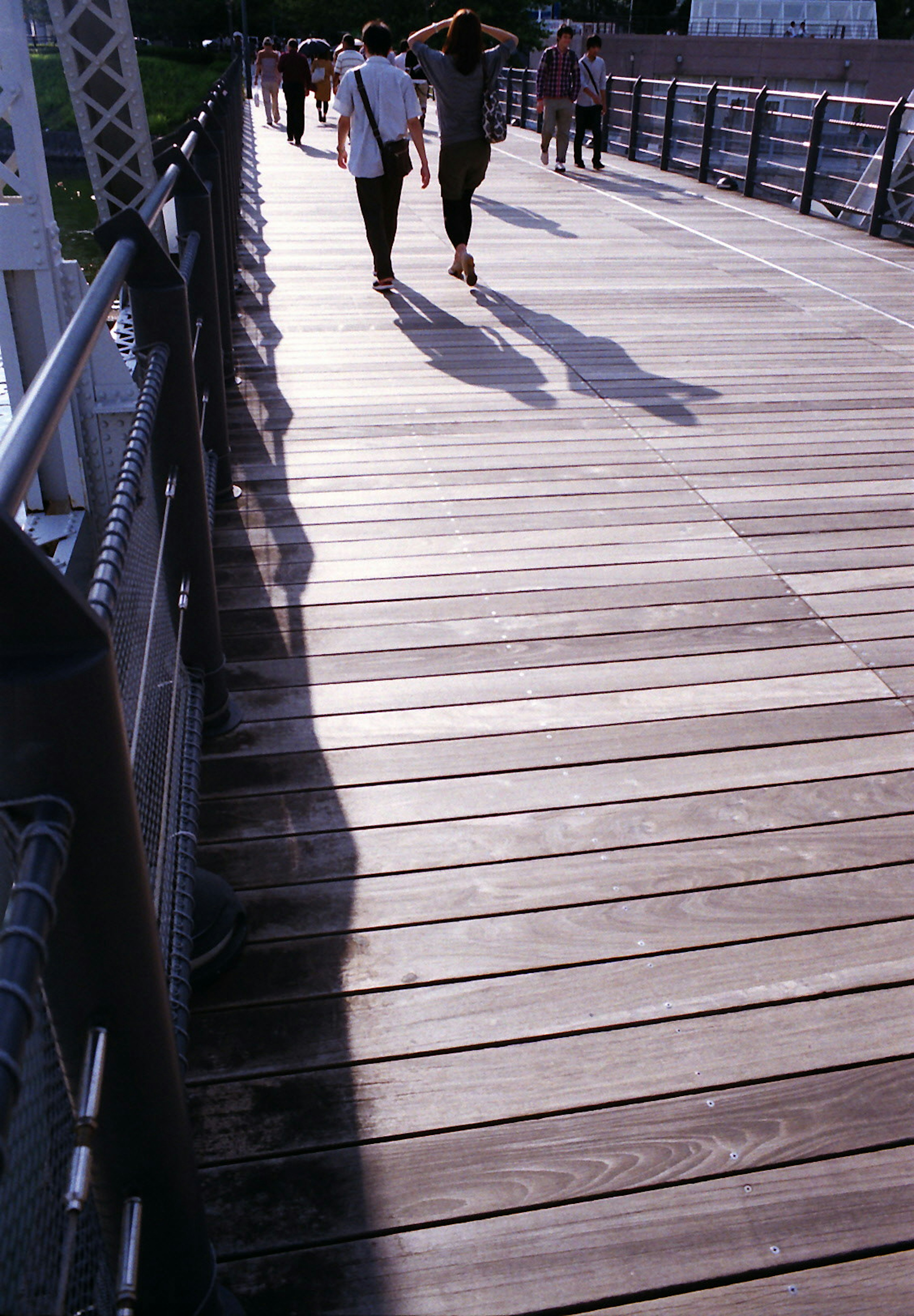 People walking on a wooden bridge with shadows cast on the planks