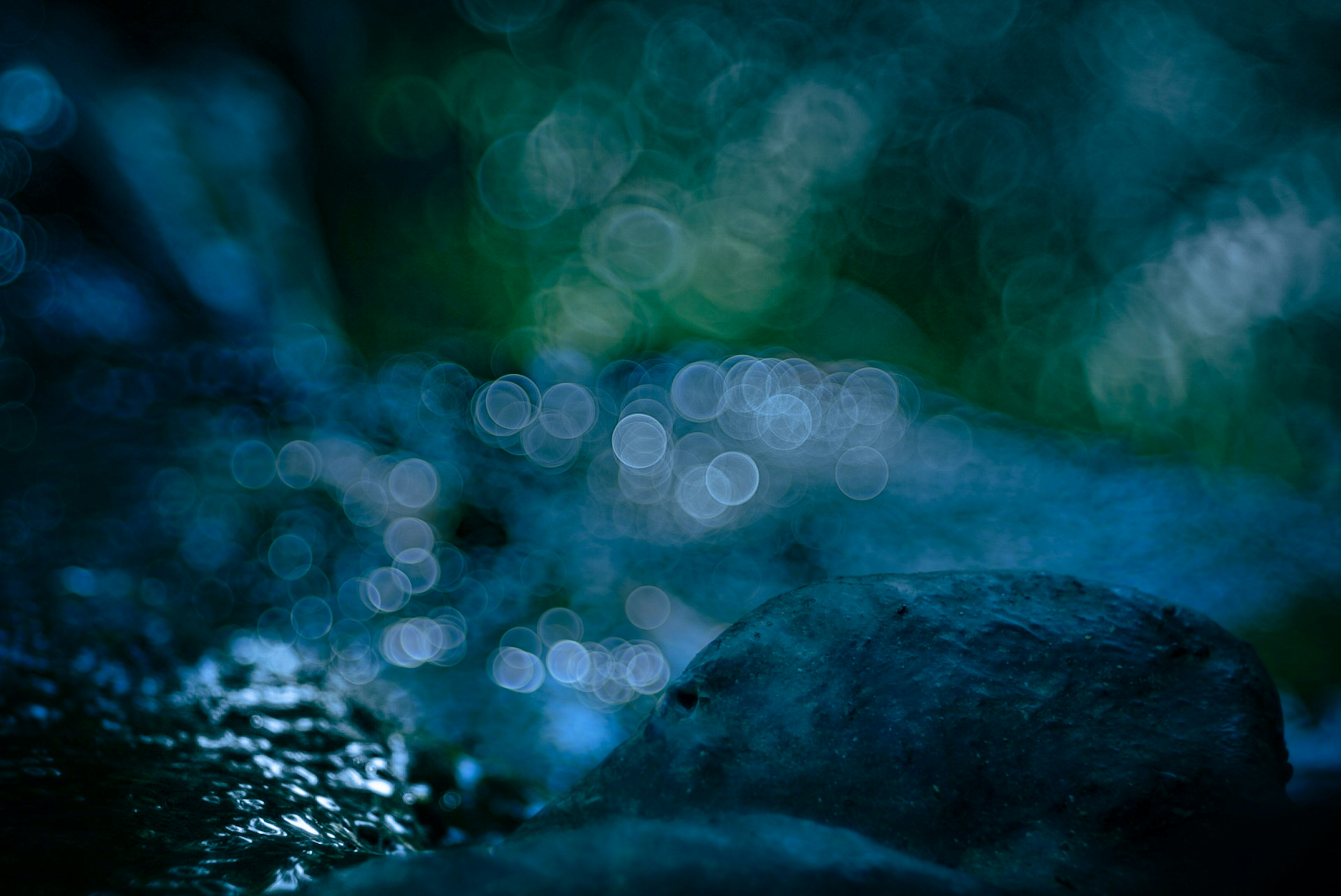 Verschwommene Bokeh-Lichter über einem dunklen blauen Hintergrund mit Steinen am Wasser