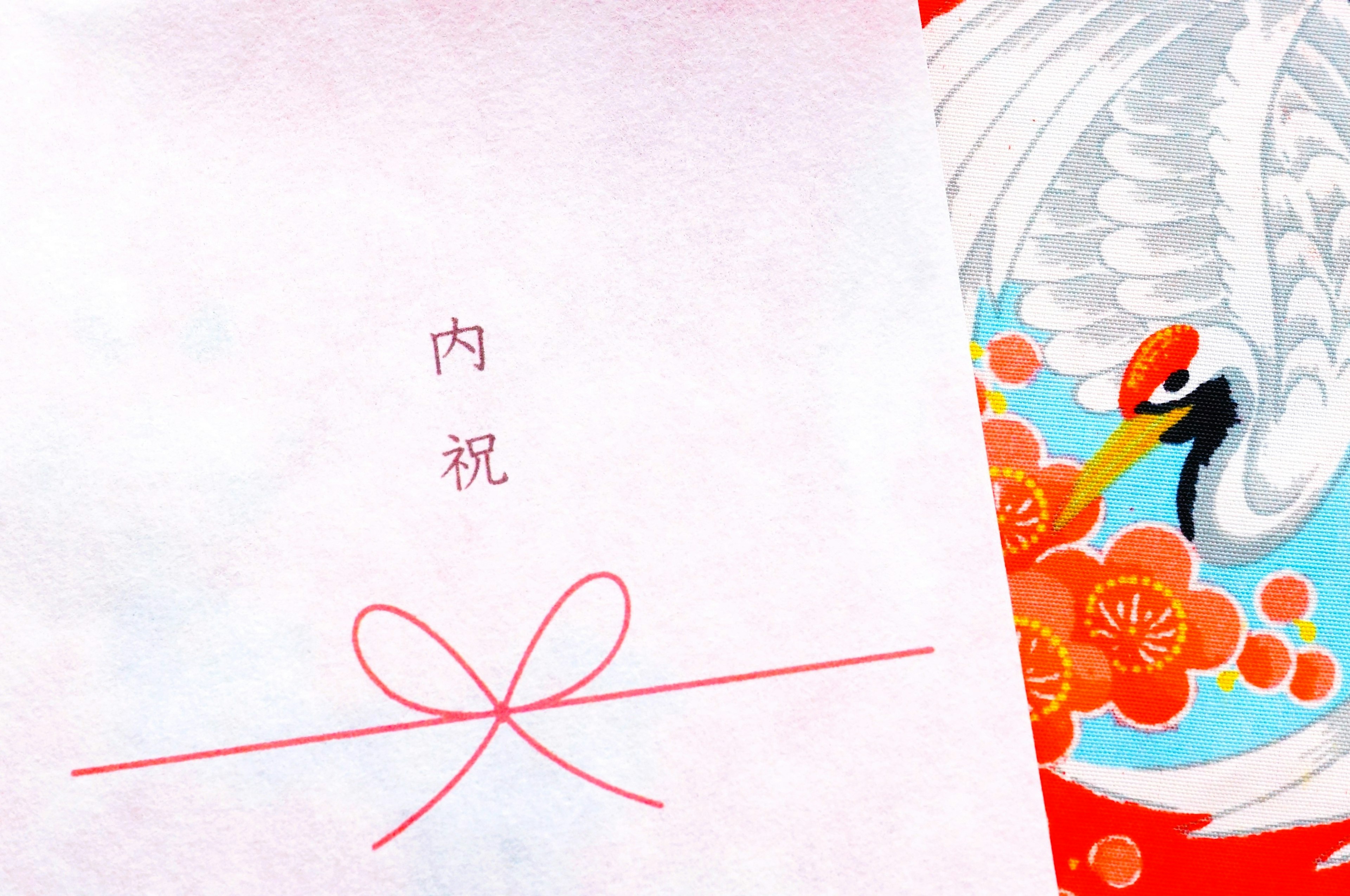 A white envelope with a red ribbon featuring the text 内祝 and a colorful crane design