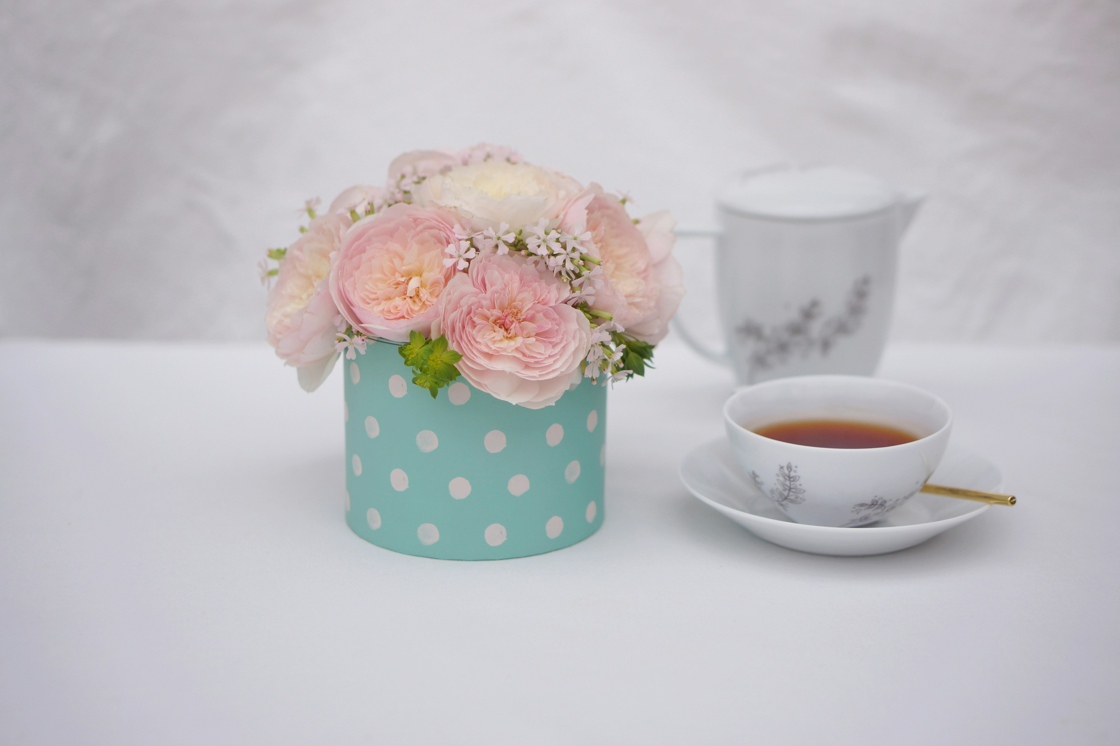 Un arrangement floral dans un vase à pois bleu avec des fleurs roses à côté d'une tasse blanche