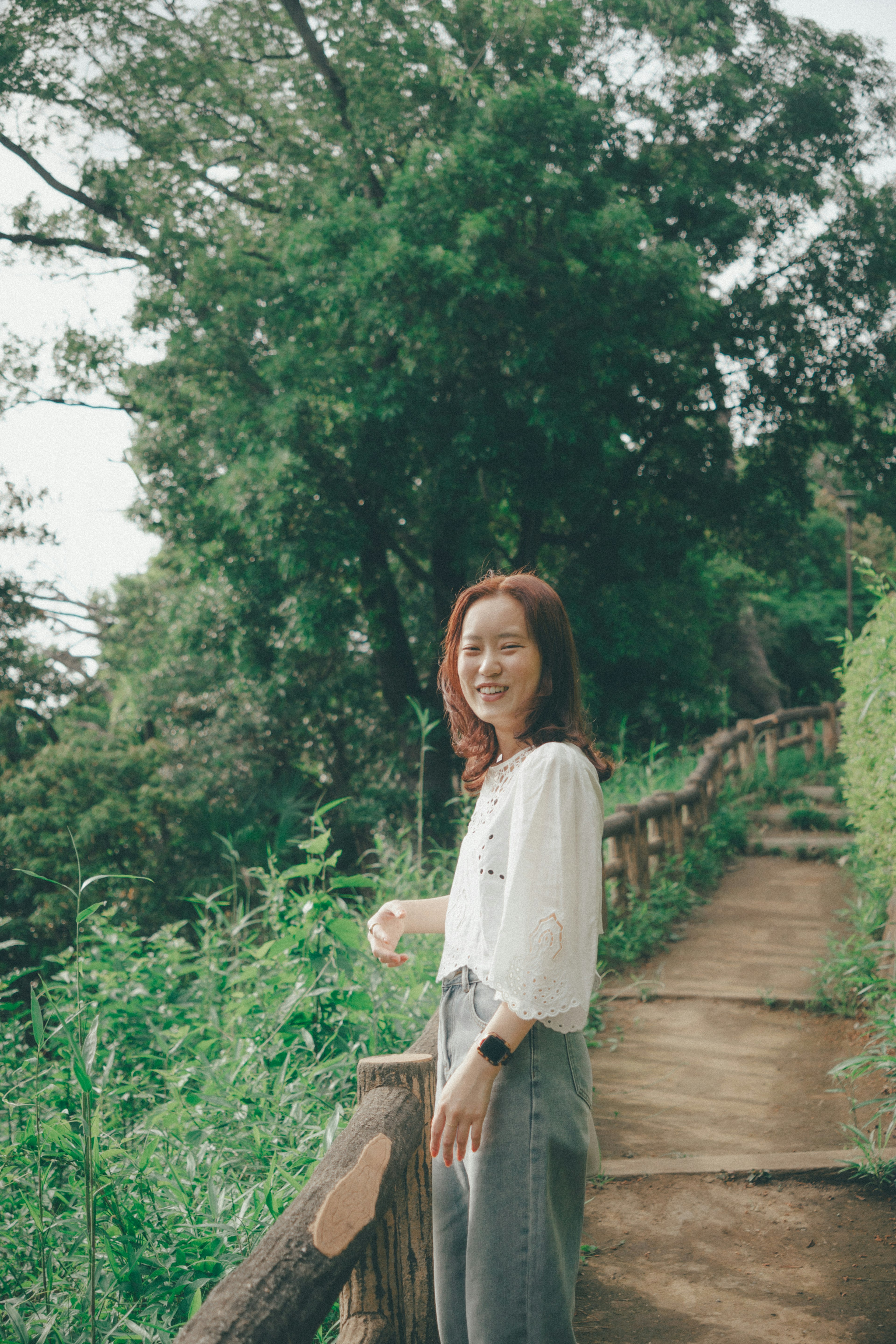 在绿色植物环绕的小路上微笑的女性穿着白色上衣和灰色裙子