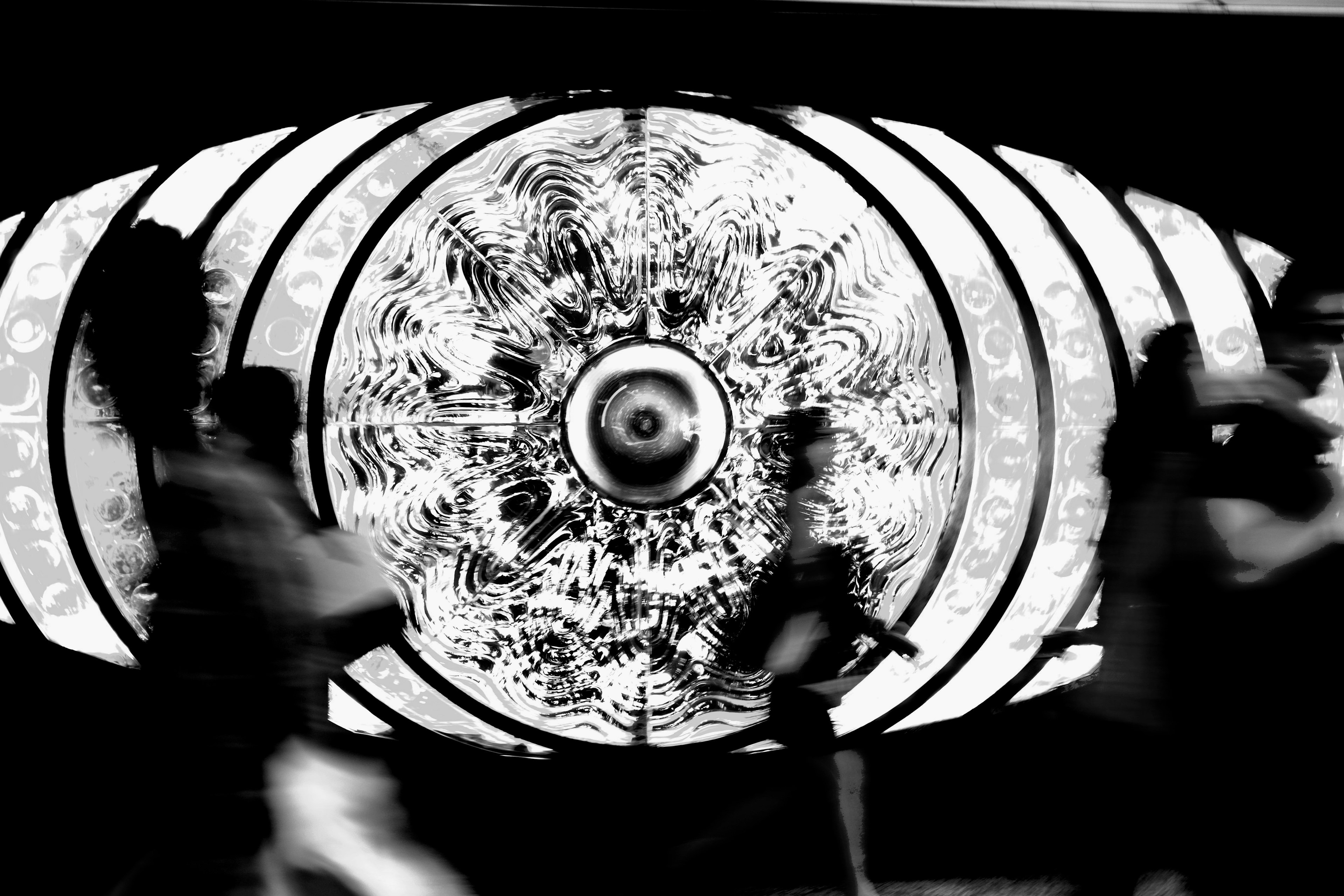 Personas caminando frente a un gran diseño de ojo en una pared en blanco y negro