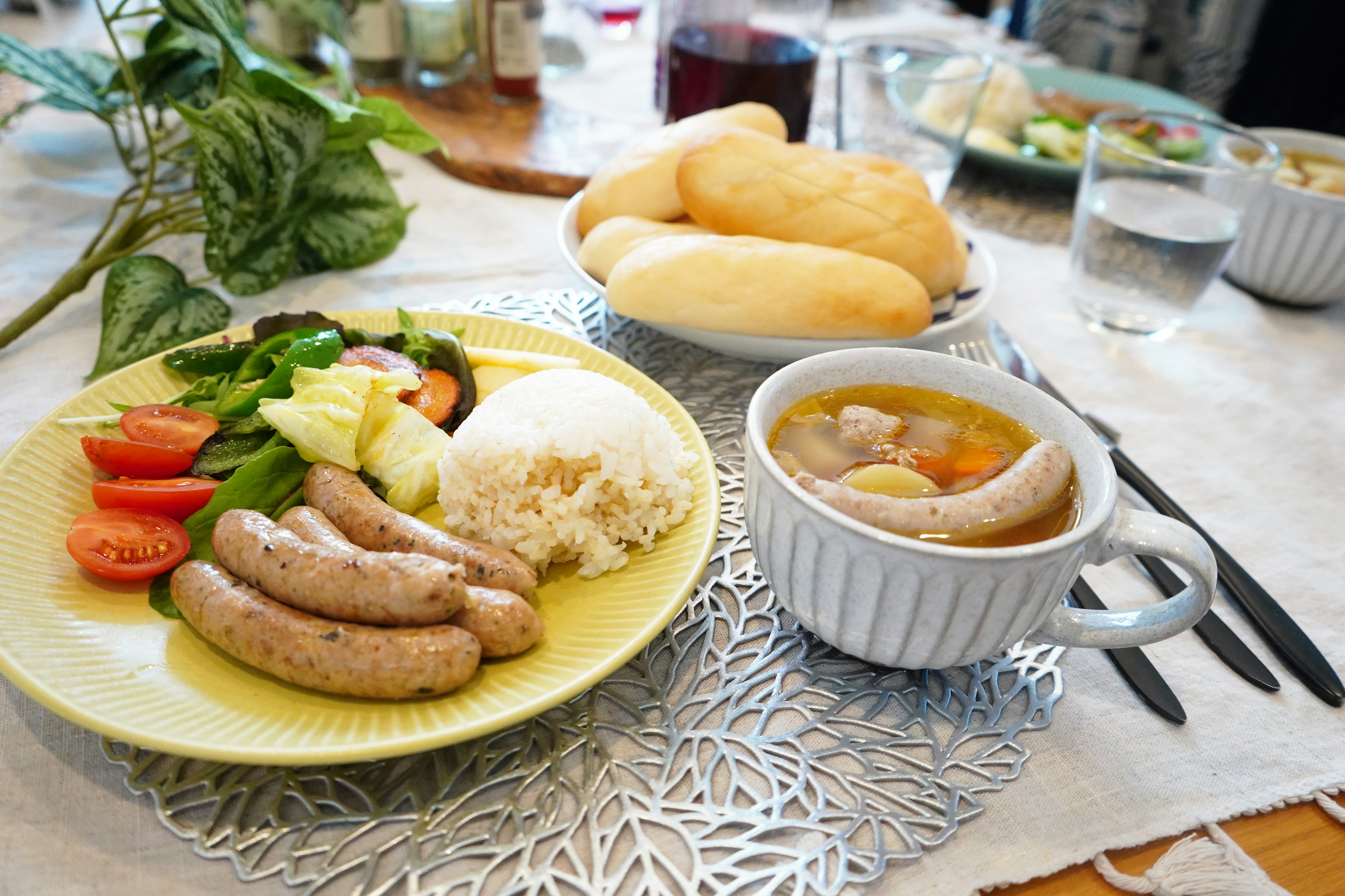 A delicious meal displayed on a table featuring sausages, salad, rice, and soup