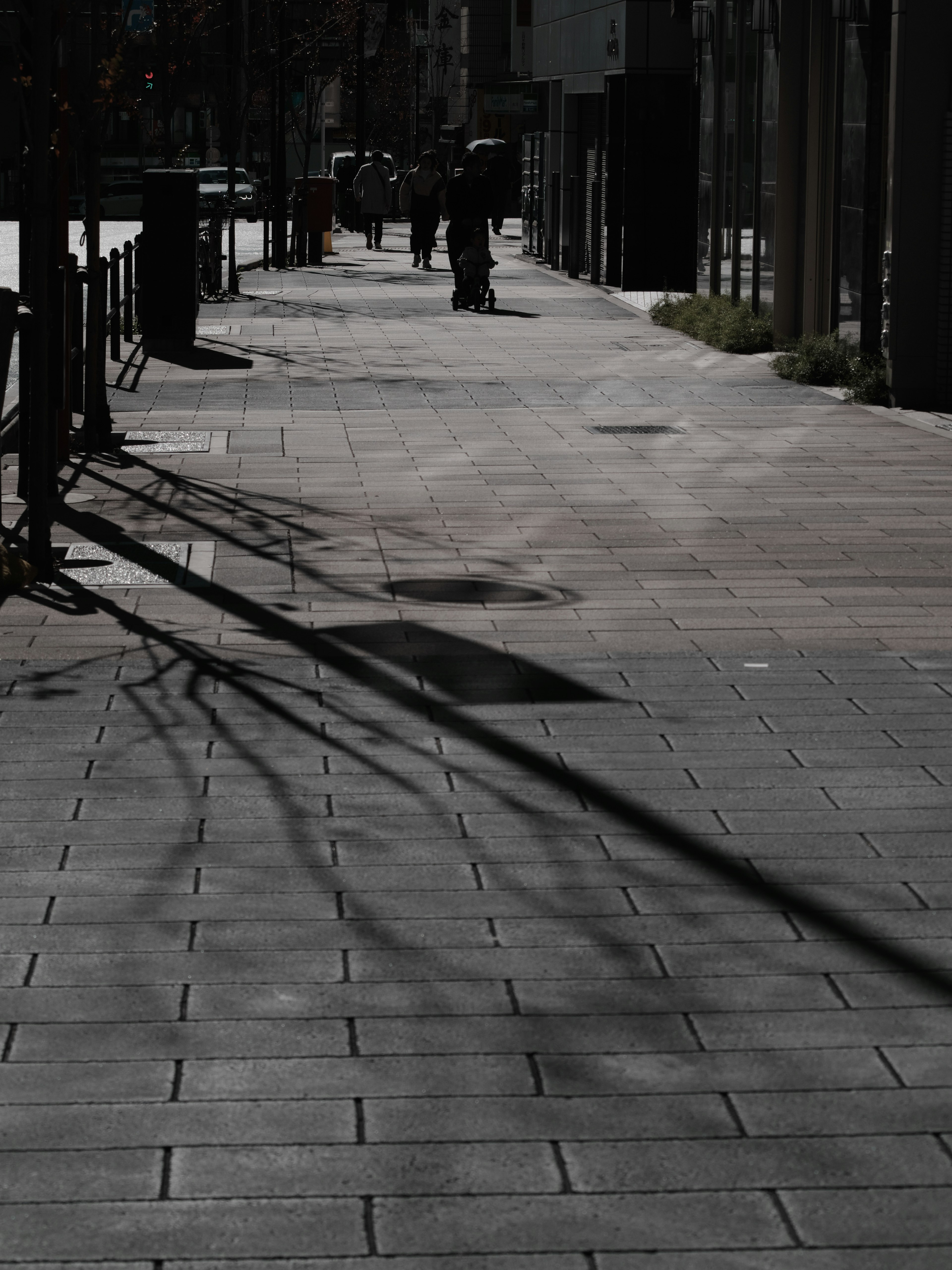 Marciapiede pavimentato con ombre e pedoni in una strada poco illuminata