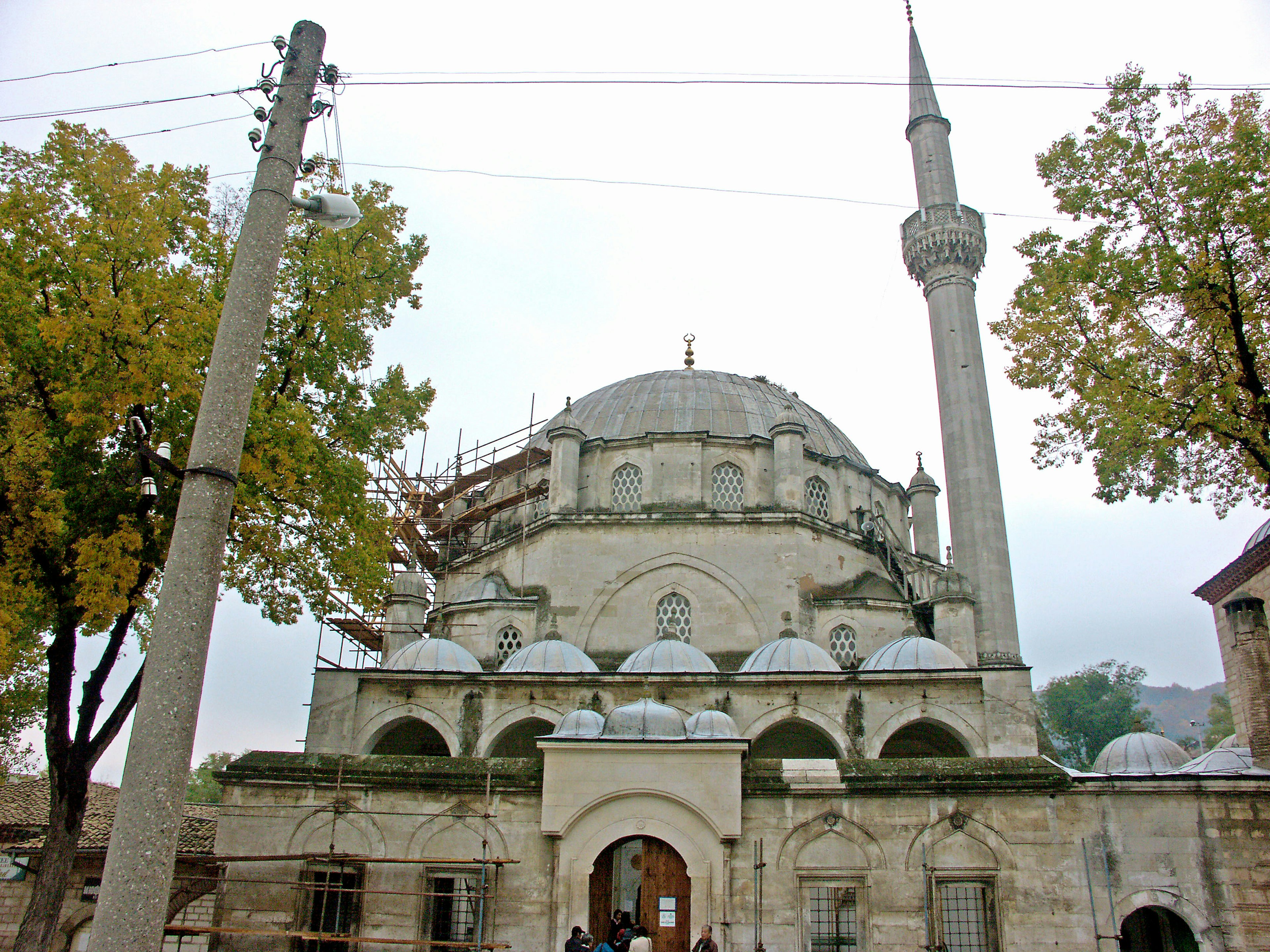 Fassade einer alten Moschee mit Minarett und umliegenden Bäumen