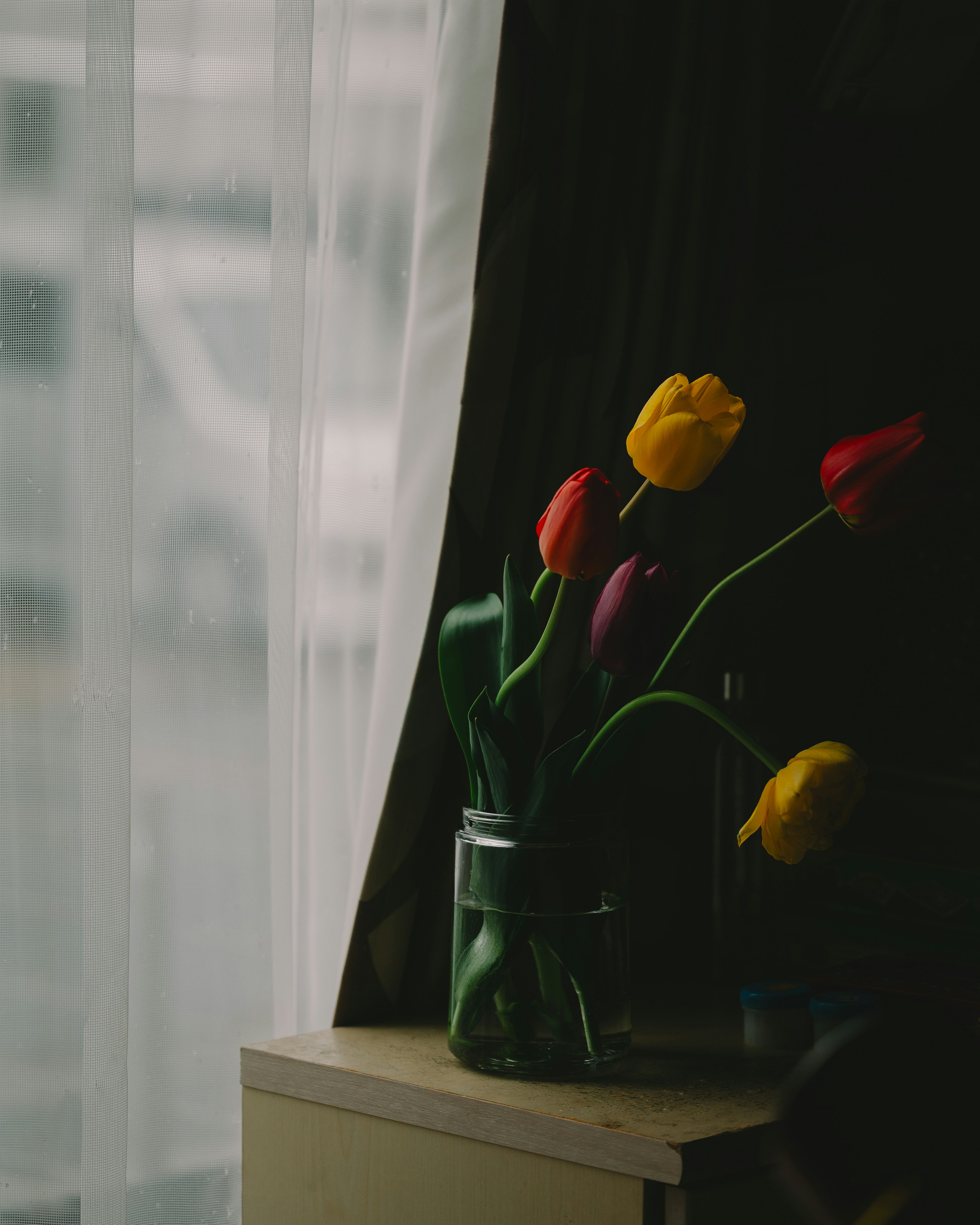 Un jarrón con tulipanes de colores colocado junto a la ventana