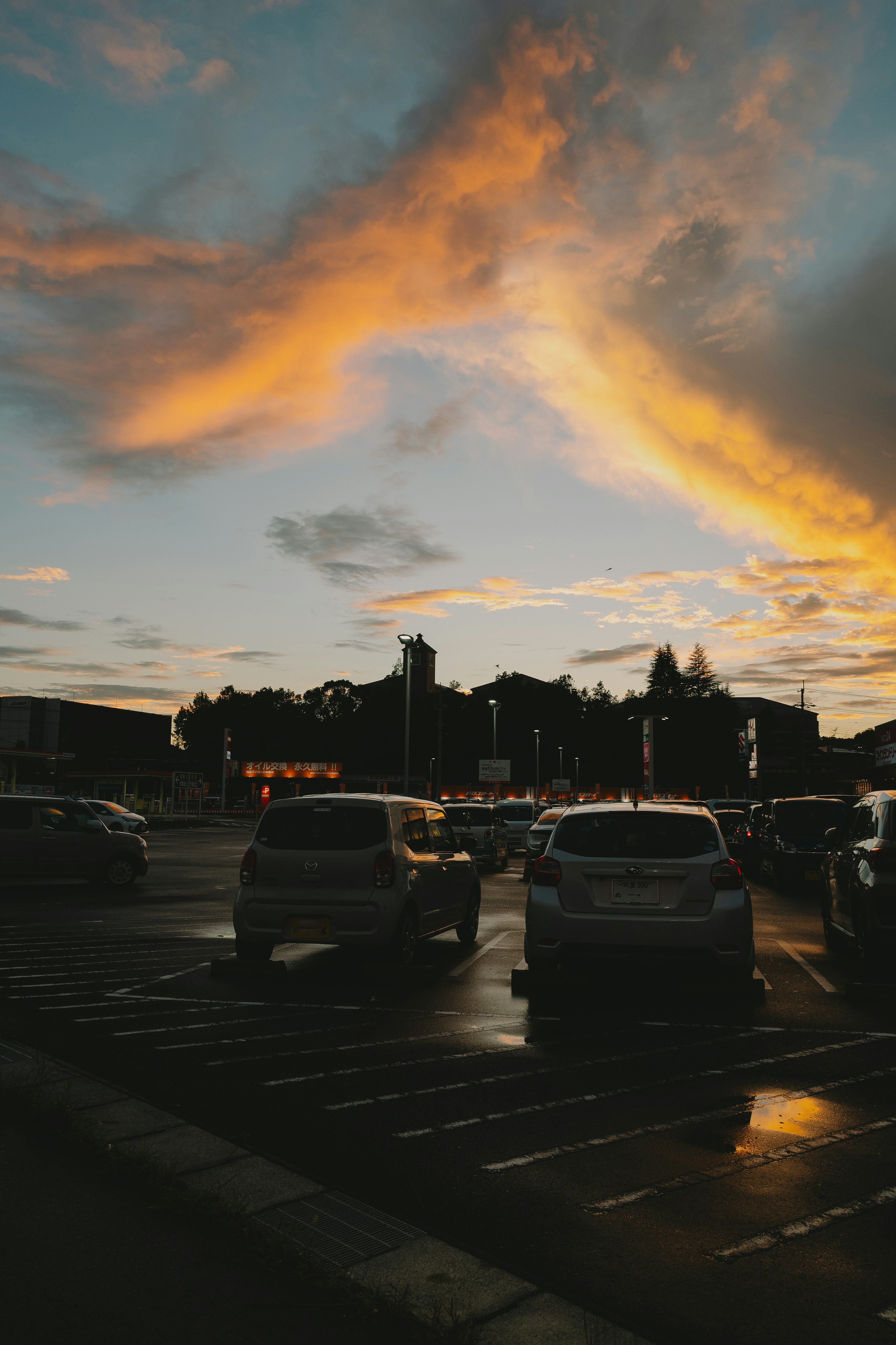 A sunset sky with colorful clouds above a parking lot filled with cars